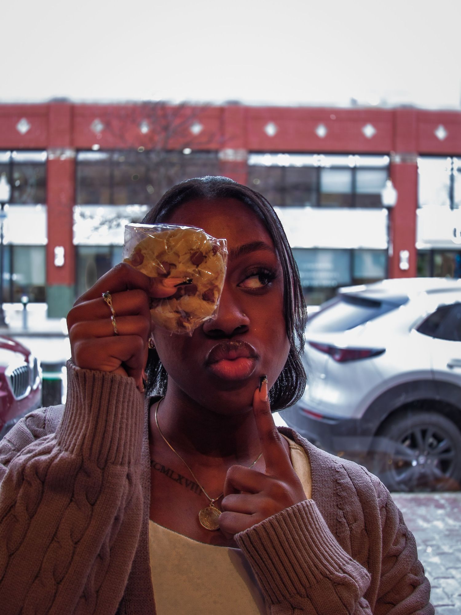 A person wearing a brown sweater makes an animated facial expression while holding a cookie.