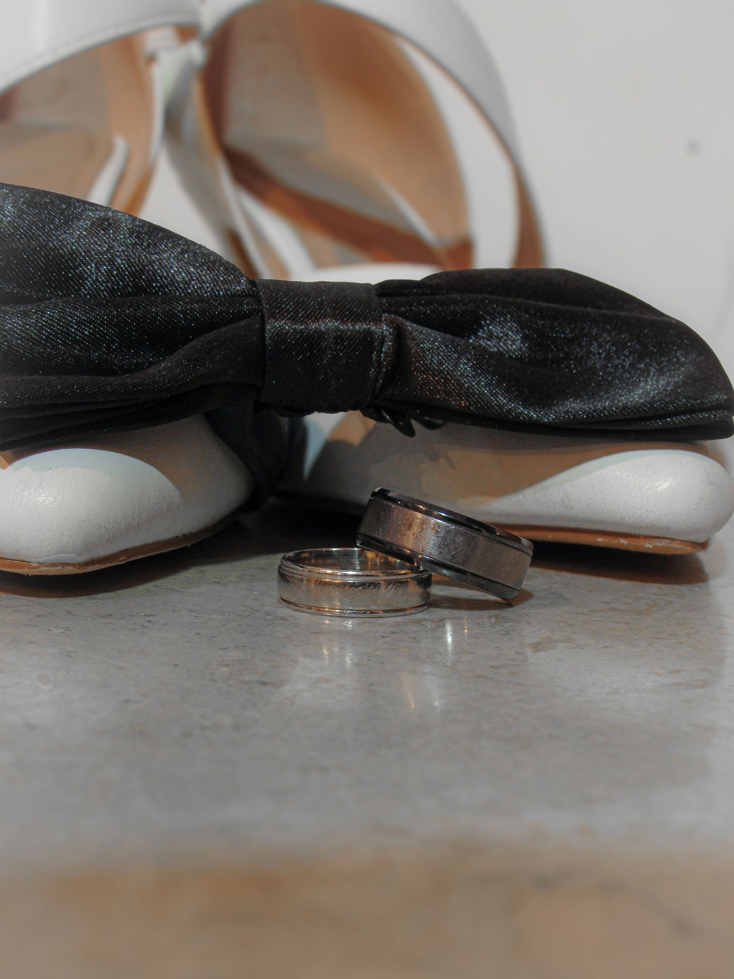 Wedding rings displayed artistically with black and white bow tie and wedding heels on a light gray textured surface.