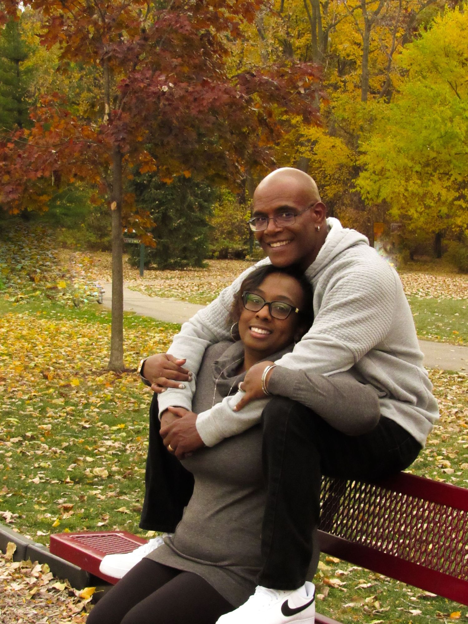 Romantic couple embracing on a park bench surrounded by vibrant autumn foliage.
