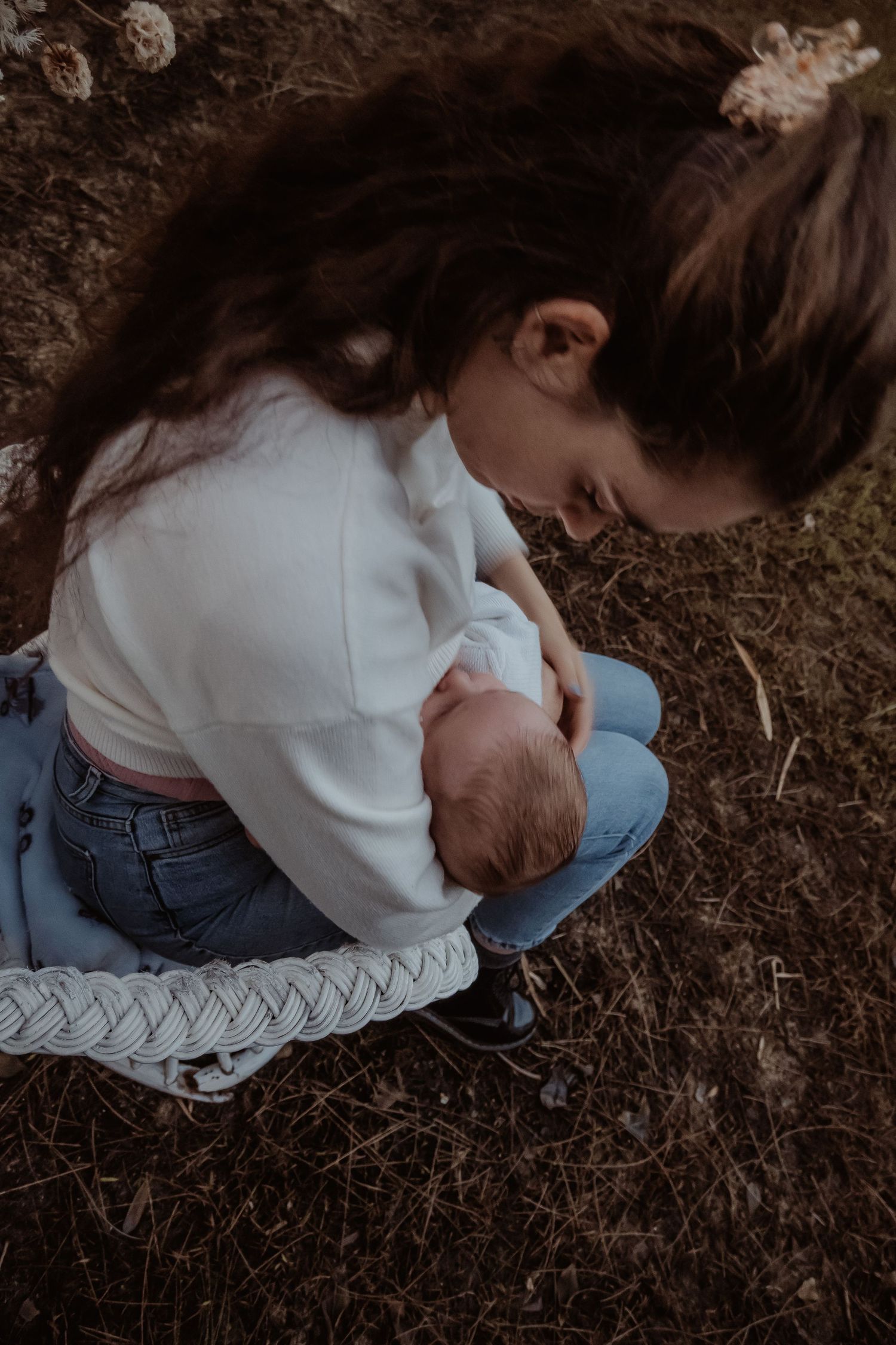 A tender moment captured shows breastfeeding outdoors wearing a white sweater and jeans at a central coast breastfeeding photoshoot.