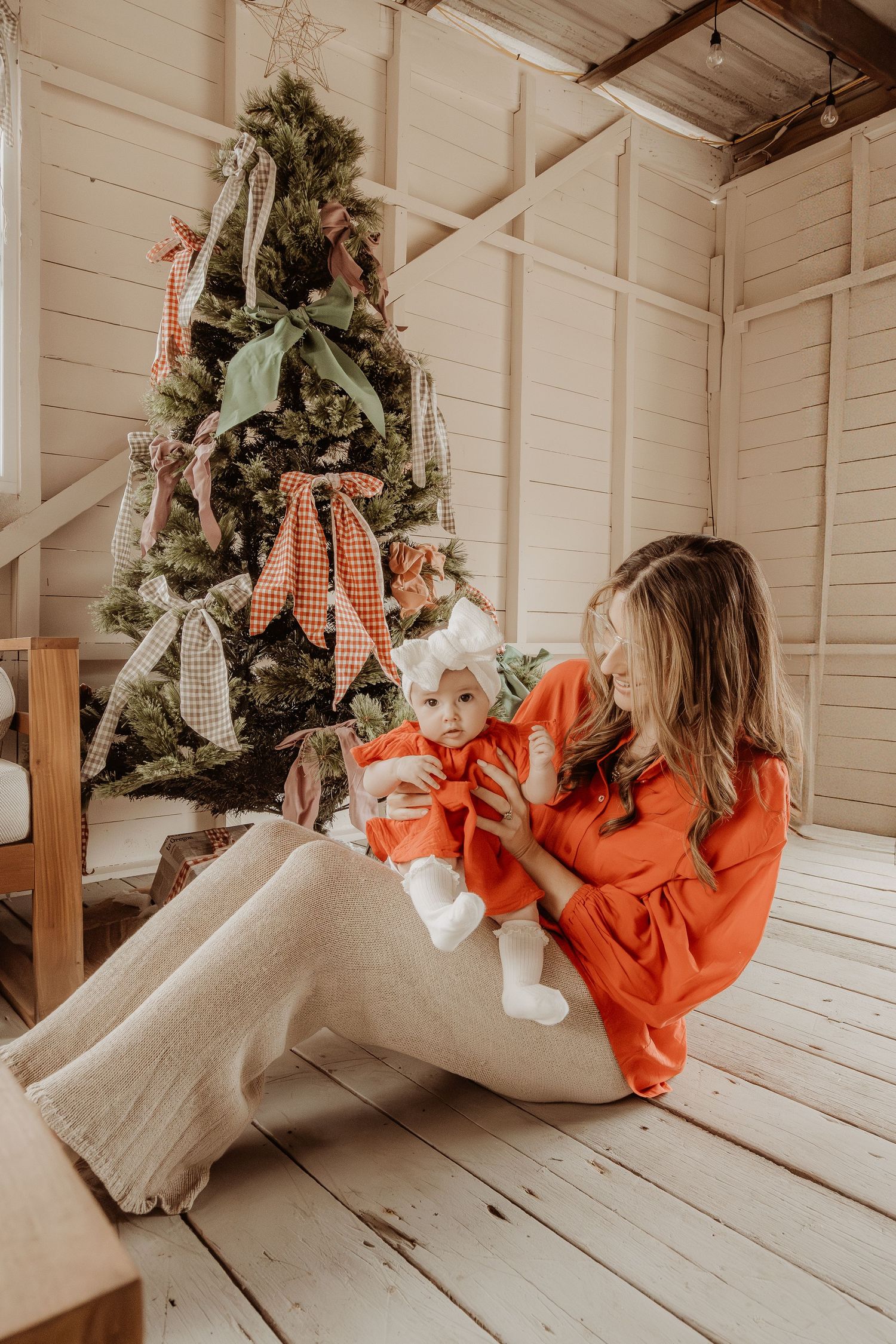 Mother playing with her daughter with decorated Christmas trees in the background at a Central Coast christmas photoshoot.