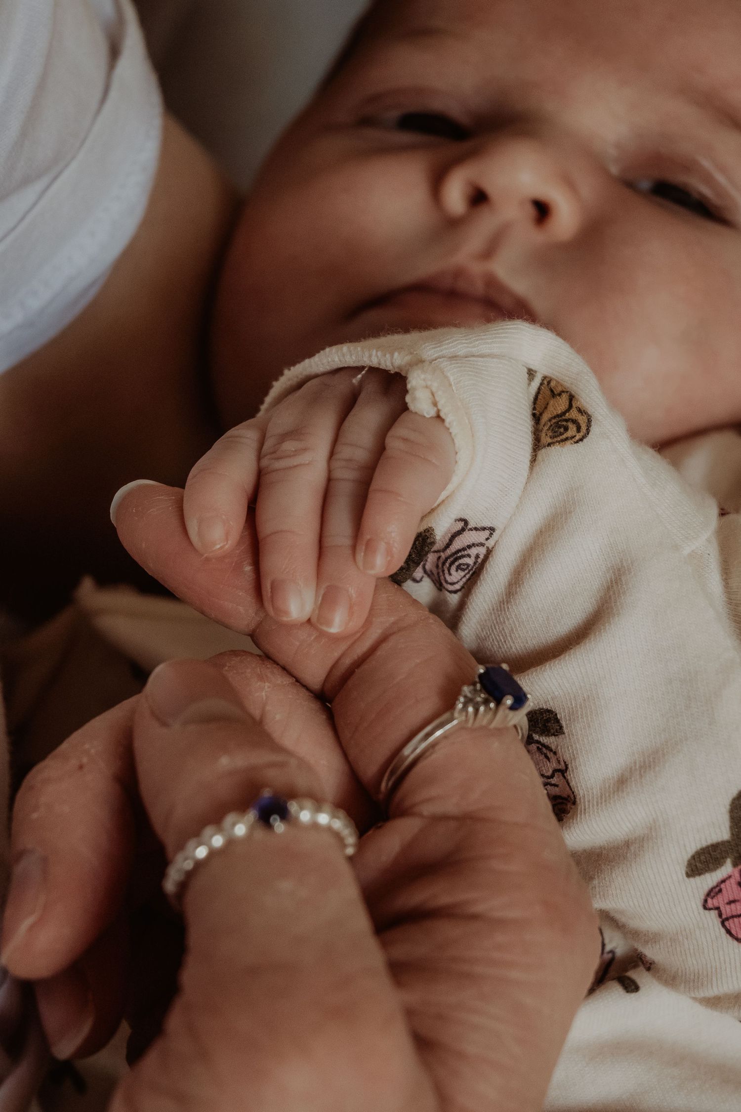 Baby's tiny hand gently held by adult wearing rings against white patterned fabric background at a central coast newborn photoshoot.