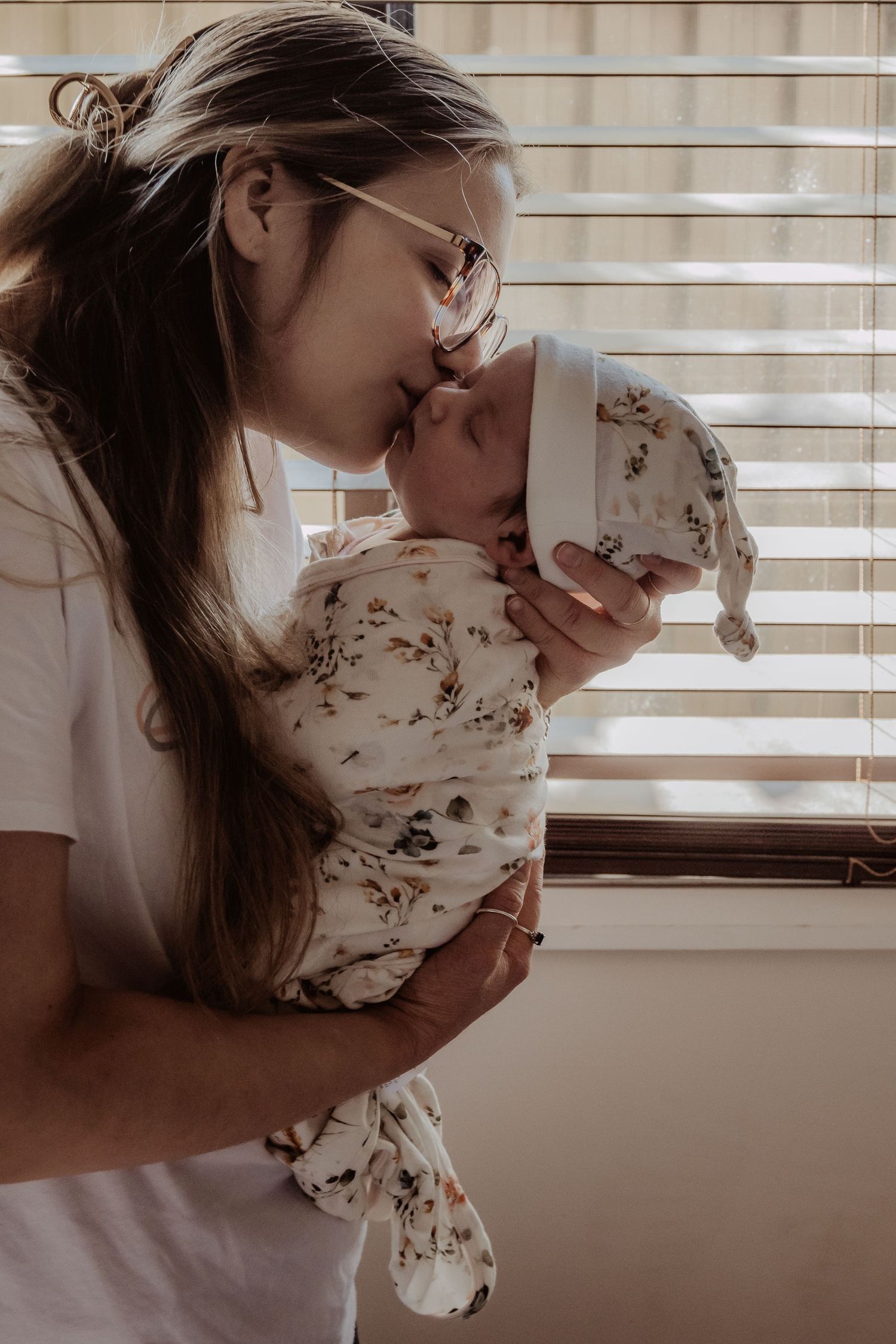 Intimate indoor portrait of parent and baby in floral swaddle by window at a central coast newborn photoshoot.
