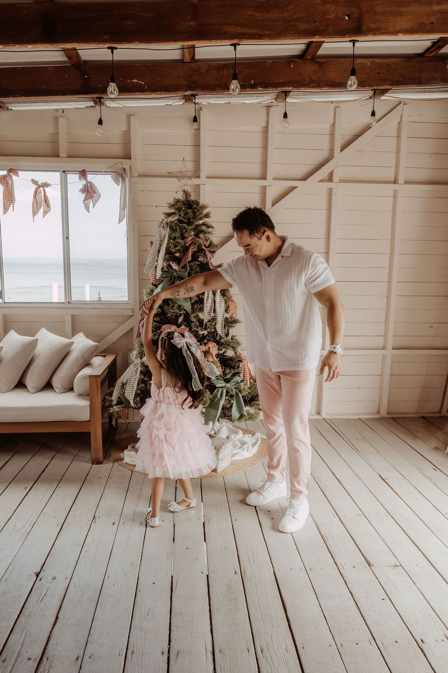 Father spinning his daughter around infront of a christmas tree at a Central Coast Christmas photoshoot.