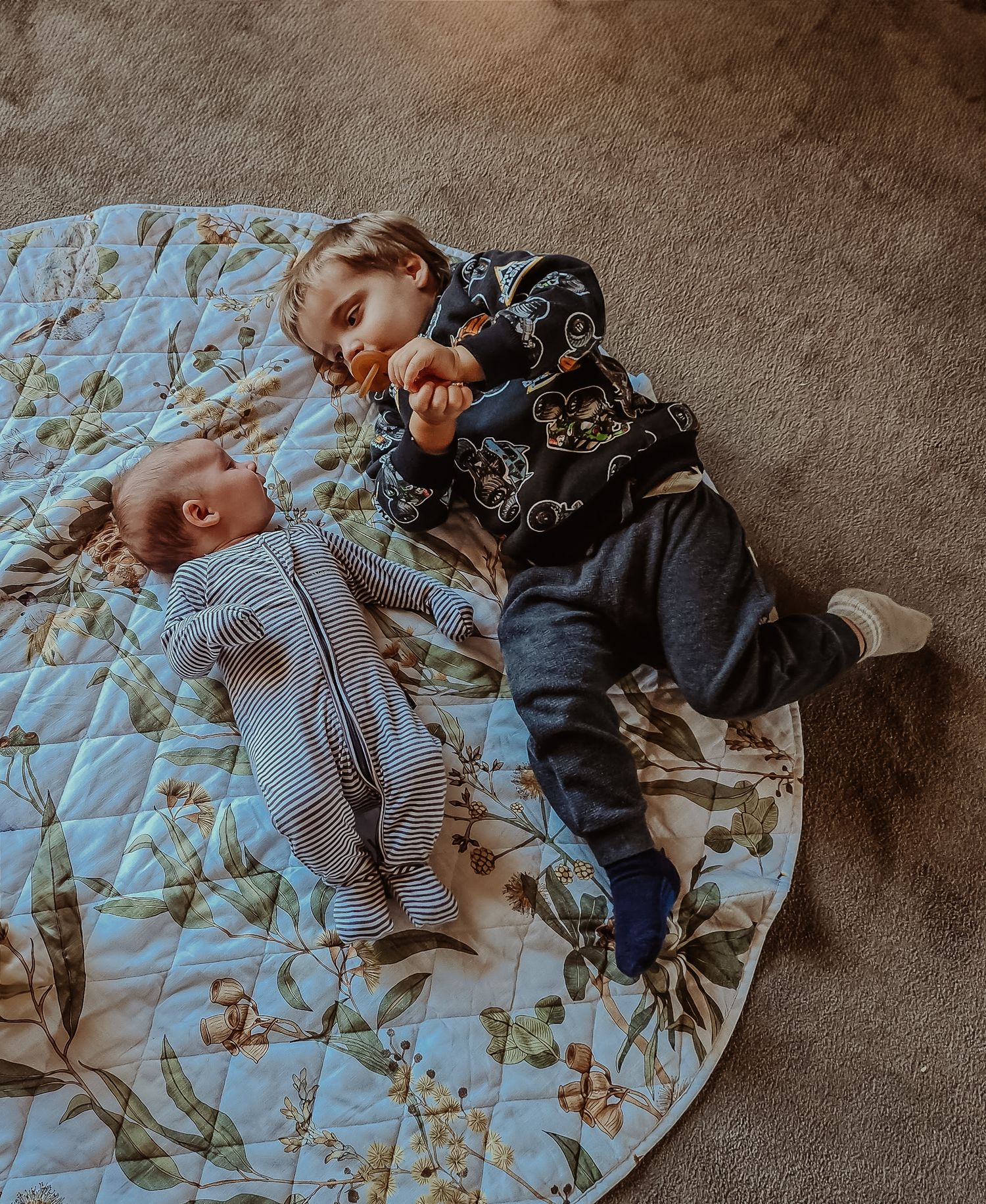 Two children lying together on a floral print blue blanket on a carpeted floor at a central coast family photoshoot.