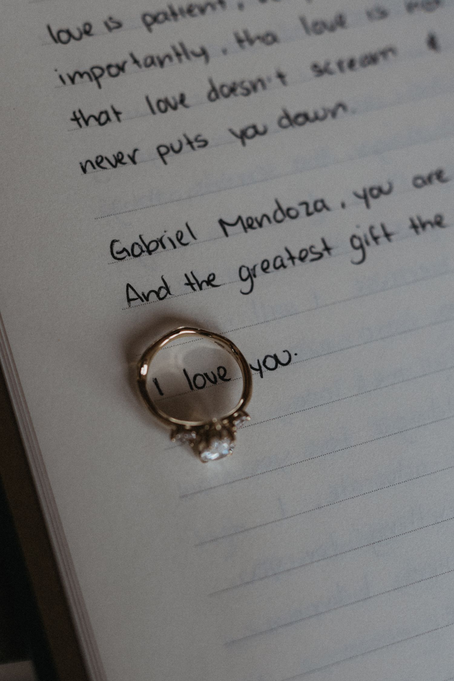 A gold diamond engagement ring resting on a handwritten love letter addressed to Gabriel Mendoza on lined paper.