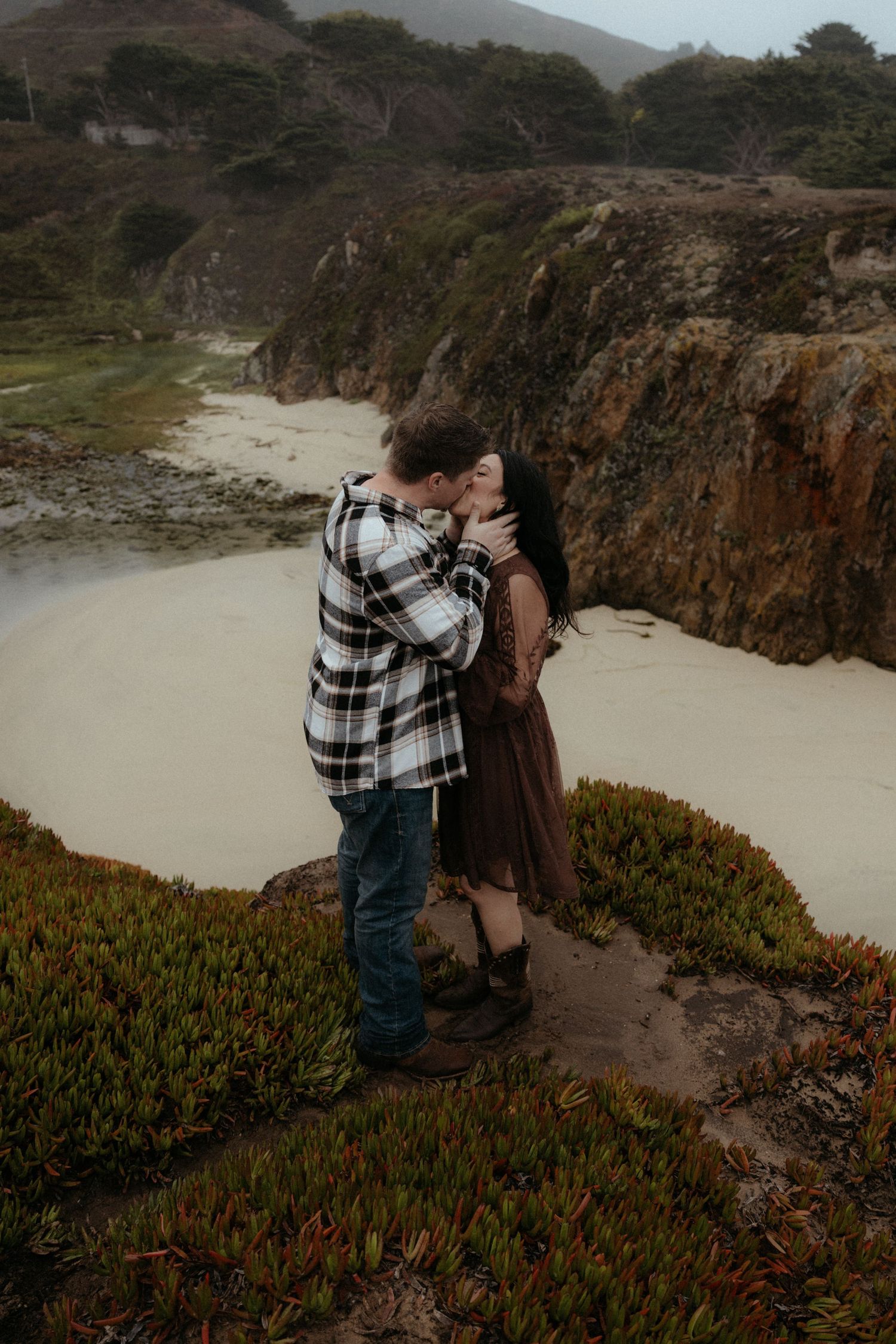 Intimate moment captured on rocky coastal path with fog rolling in over the cliffs.