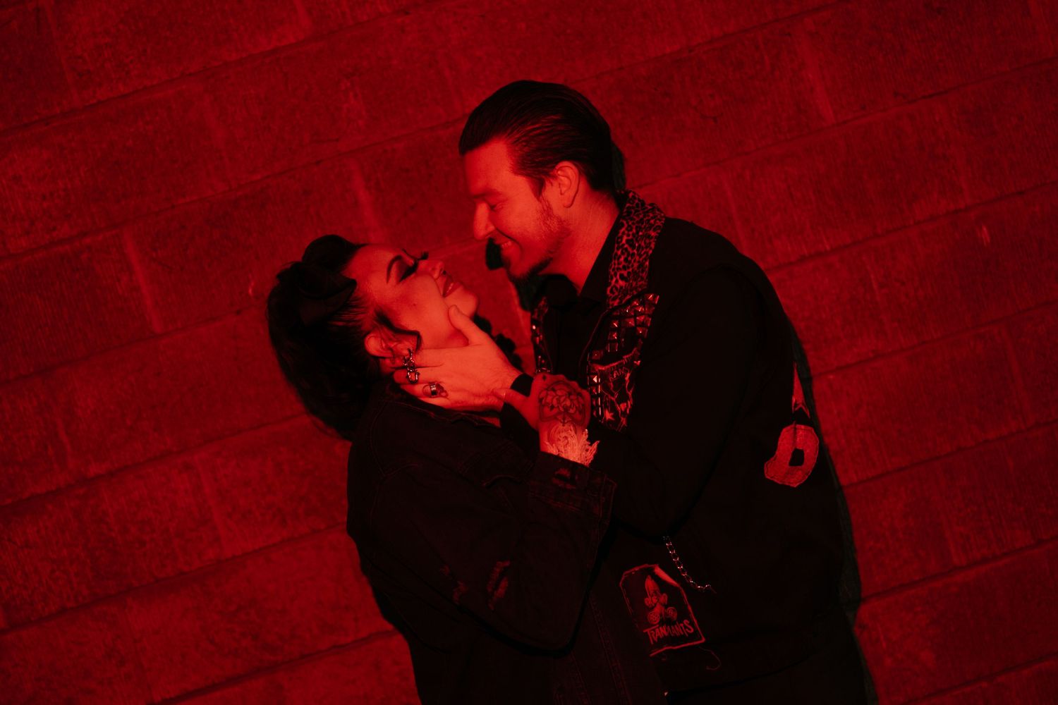 A couple embraces in dramatic red lighting against an industrial backdrop.