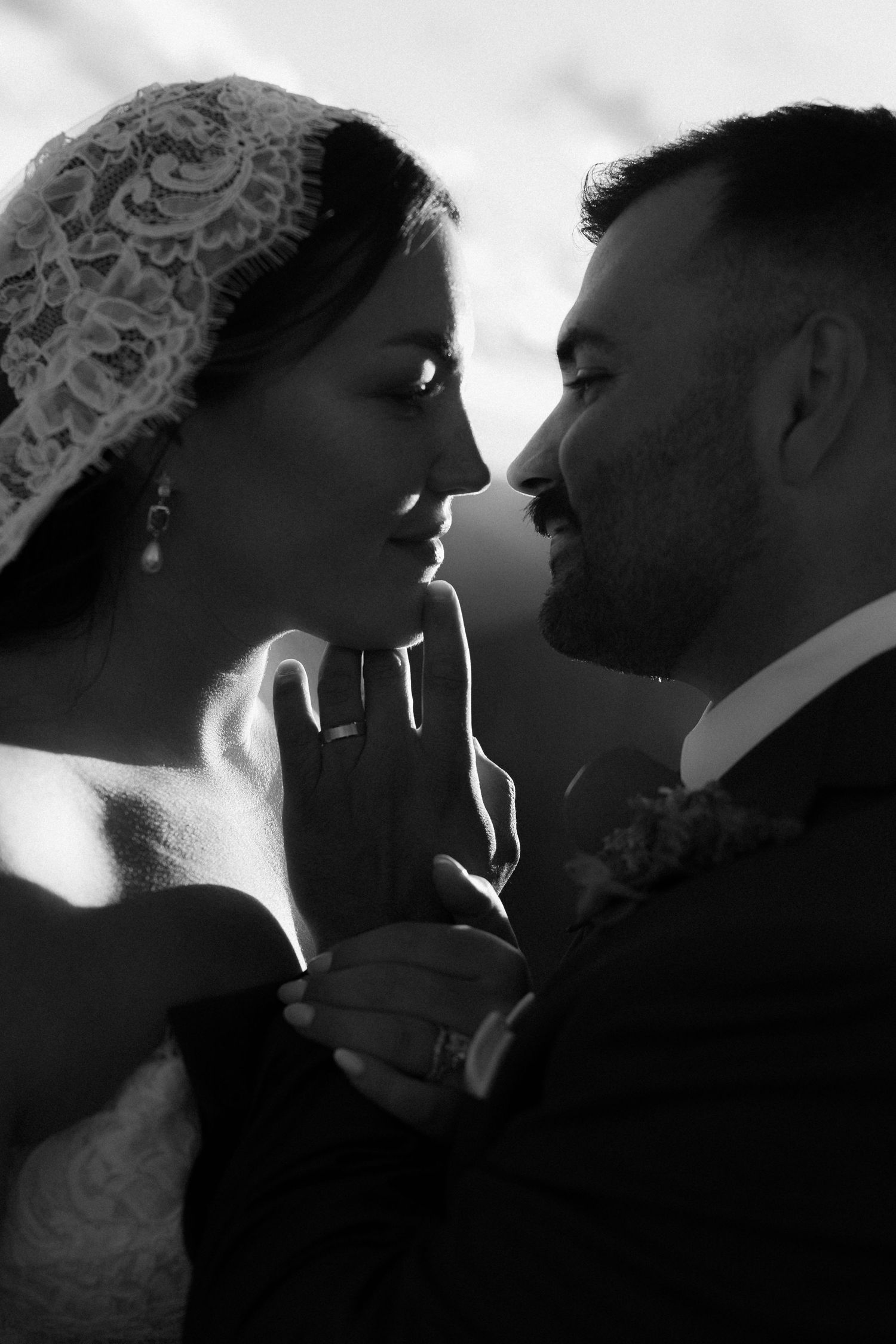 Black and white wedding portrait of bride and groom gazing at each other, bride wearing lace veil.