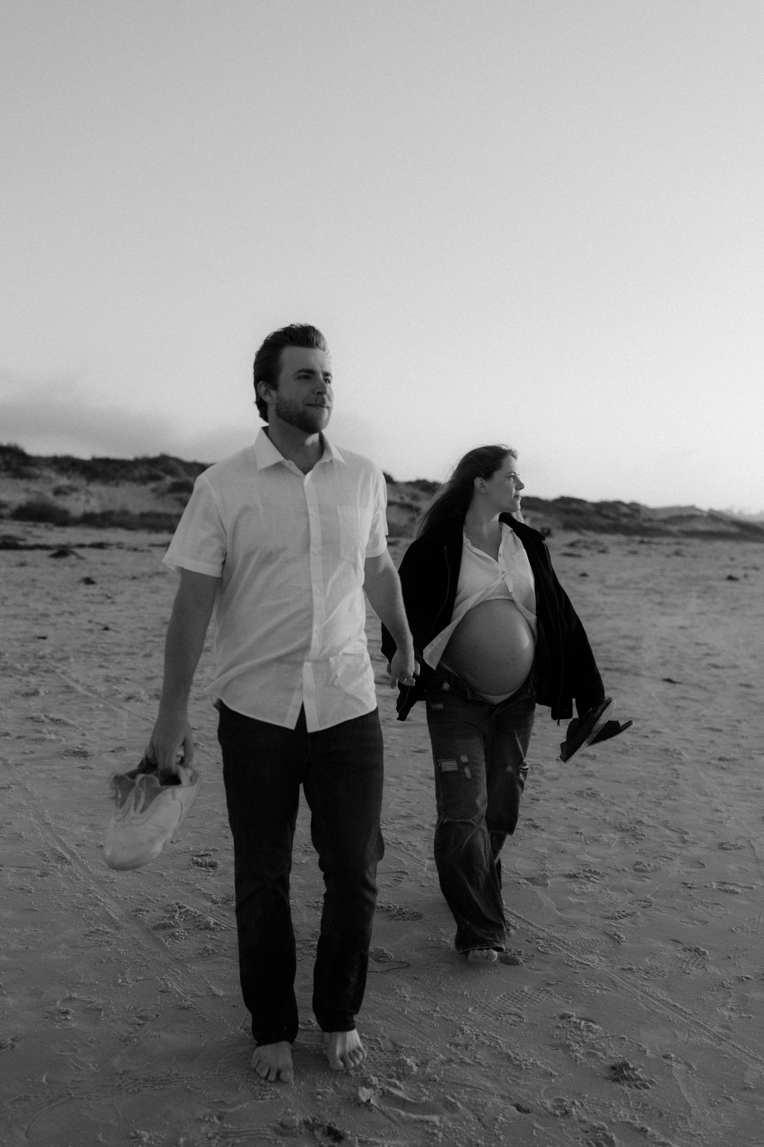 Black and white photo of couple walking together on sandy beach at sunset.