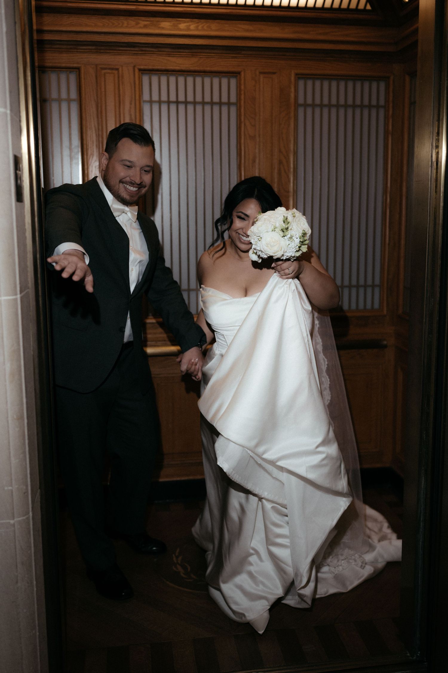 A couple playfully walks through an elegant hallway with wooden paneled walls.
