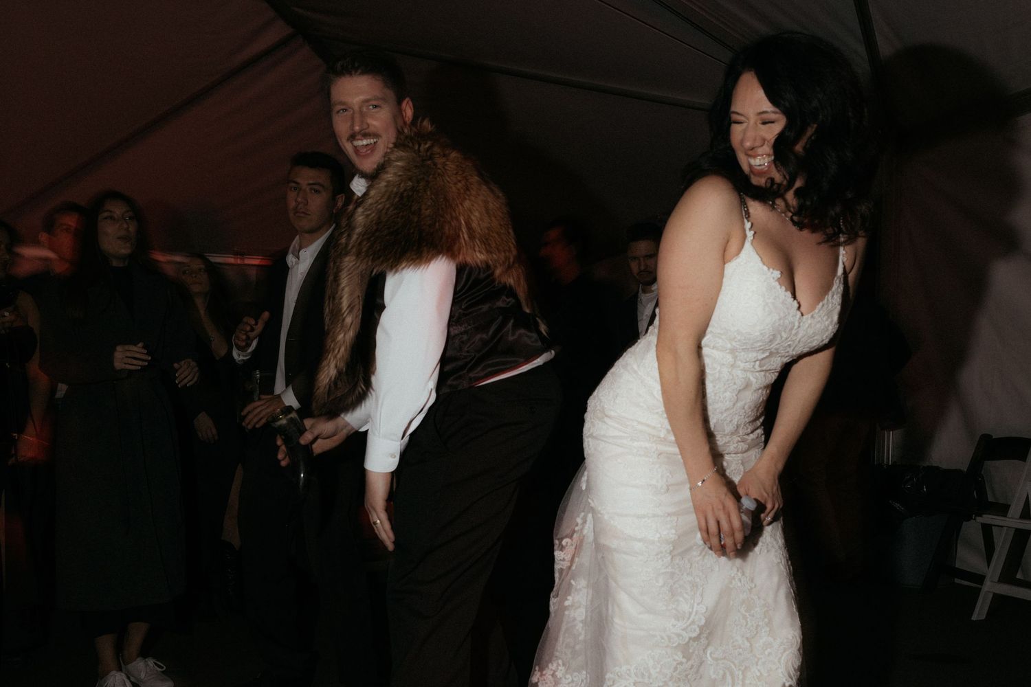 Newlywed couple shares their first dance at a wedding reception surrounded by guests in a dimly lit venue.