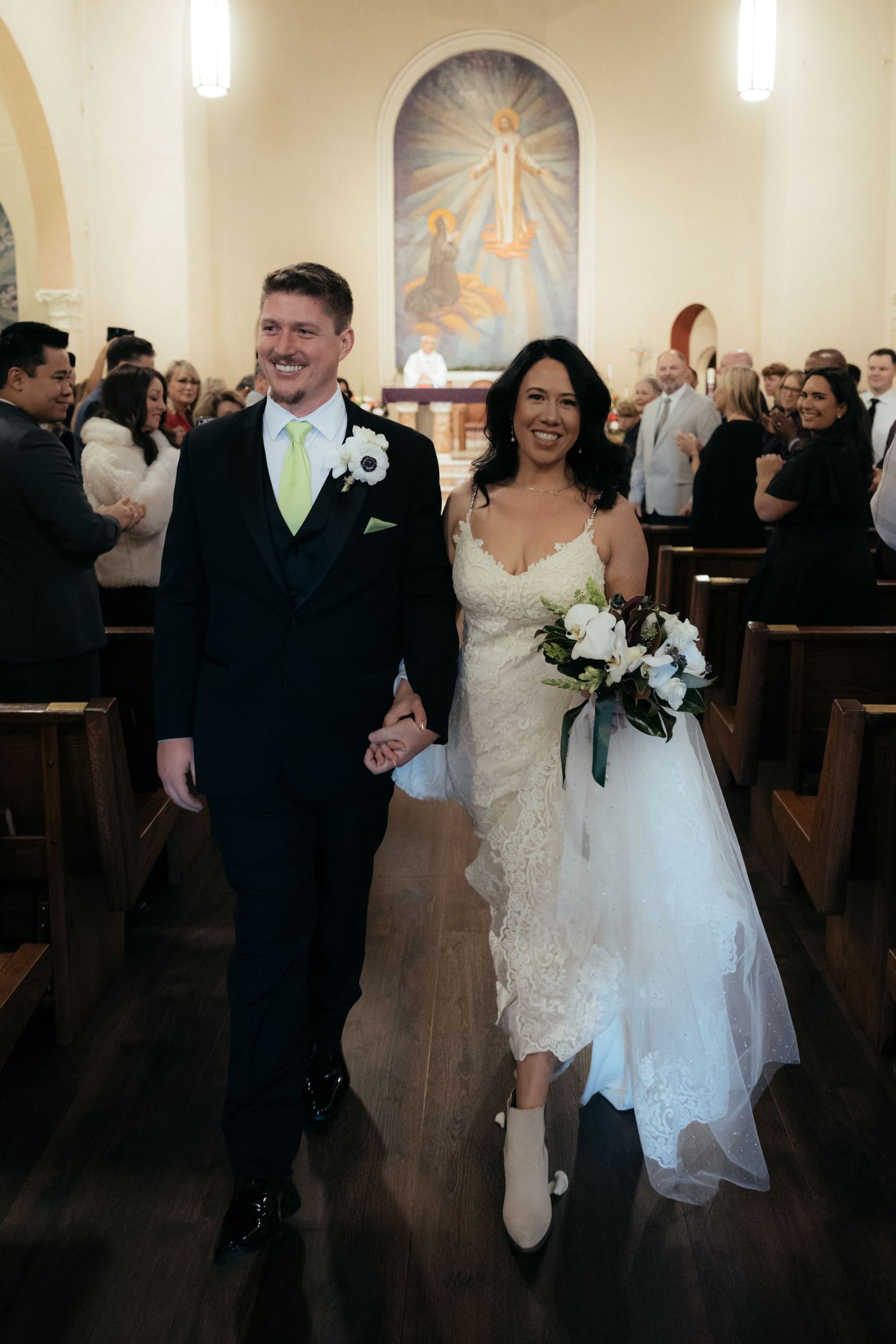 Newlyweds celebrate with guests in a church venue featuring warm lighting and decorative sunburst wall designs.