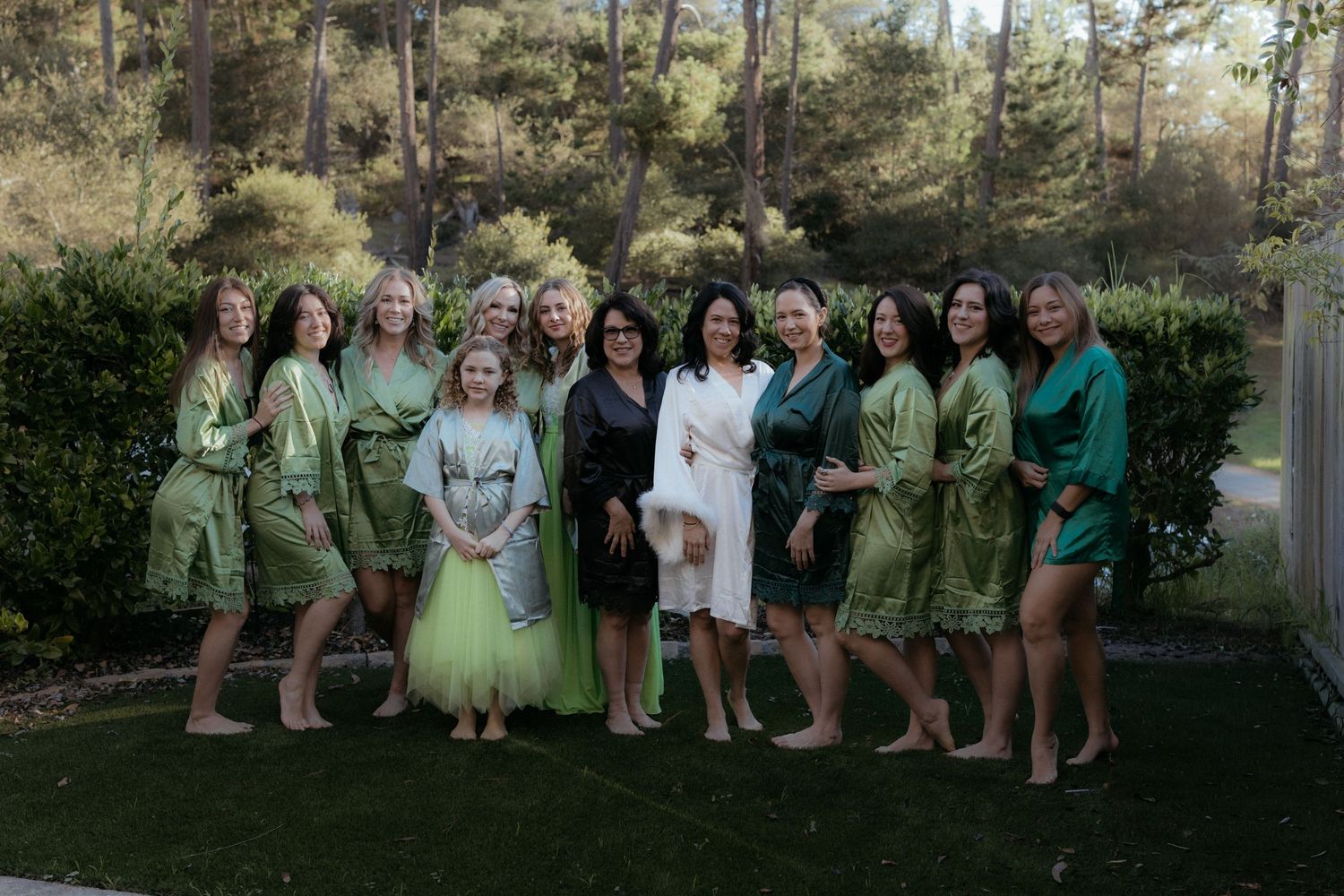 Group photo outdoors with people wearing matching green and white robes standing on grass with trees in background.