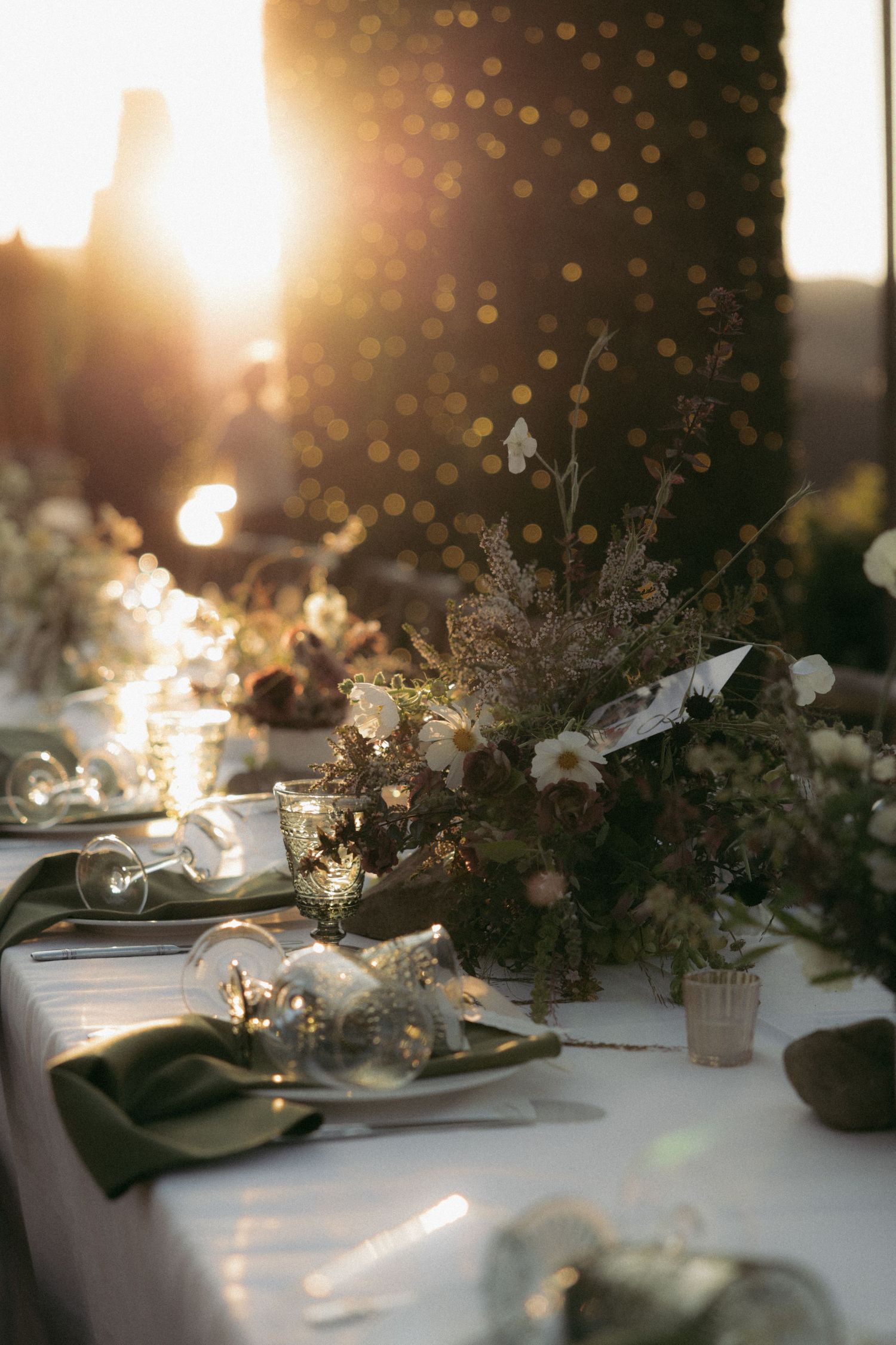 Elegant wedding table setting with floral centerpieces and candles glowing in golden sunset light.