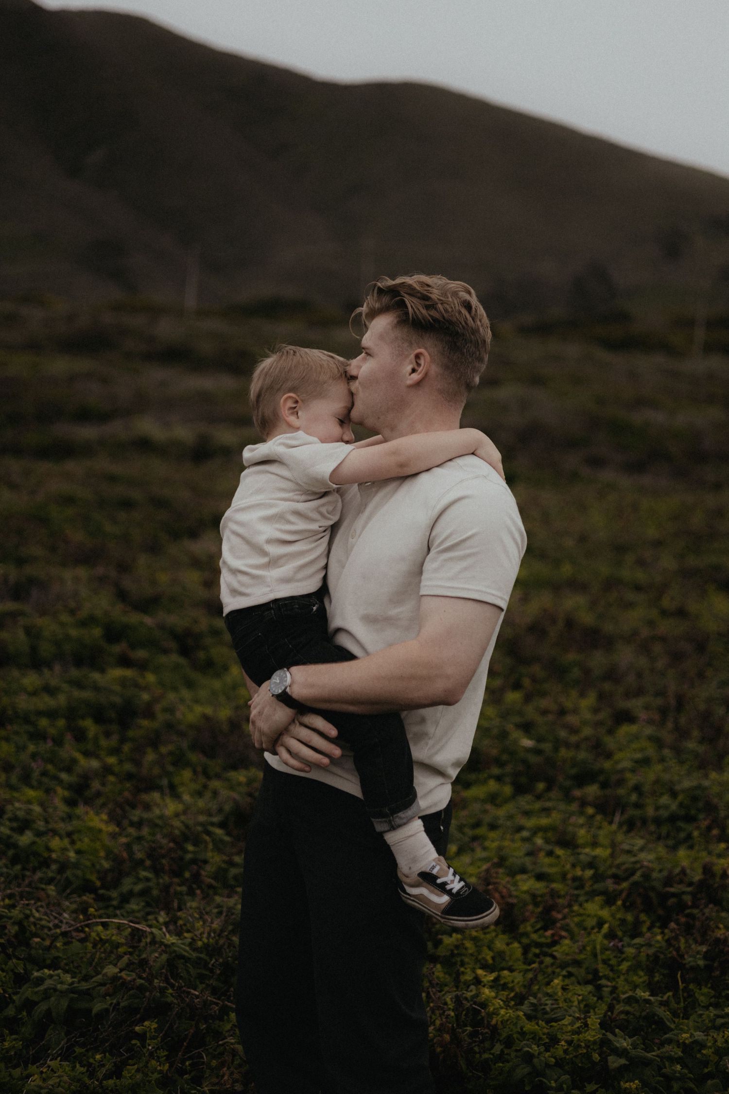 A tender family embrace captured in a moody outdoor setting with mountains in the background.
