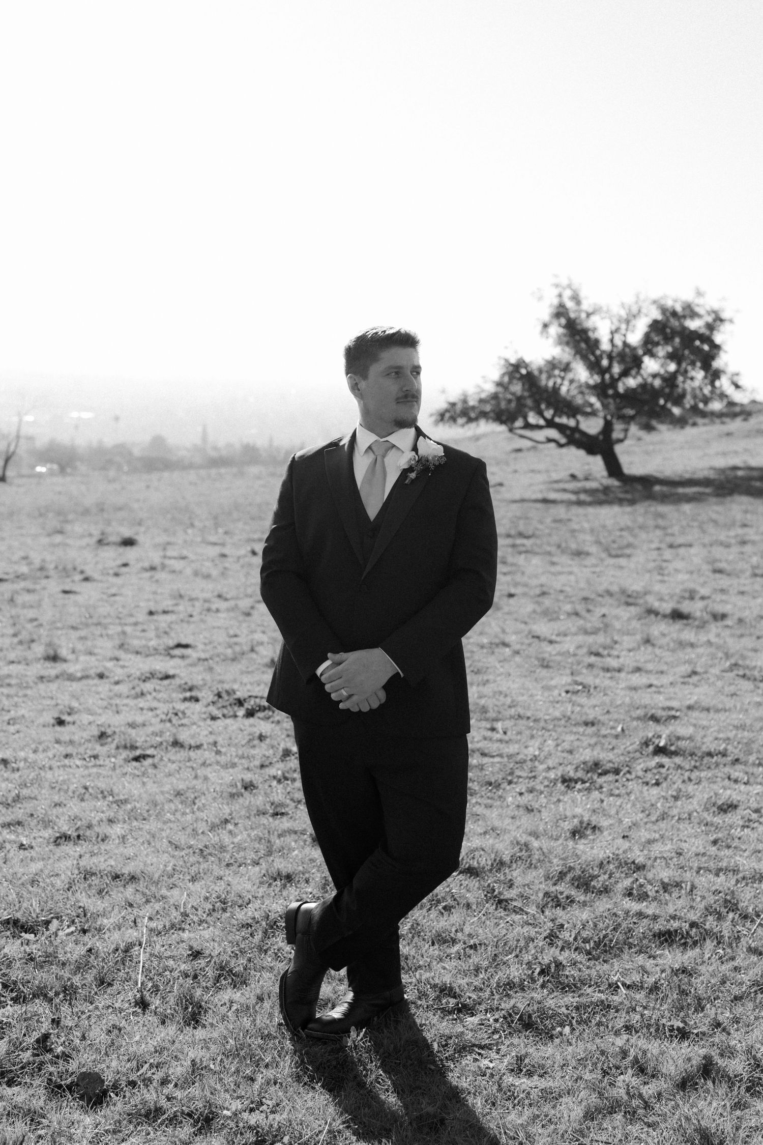 Artistic black and white portrait series of a groom in a classic suit against a minimalist landscape.