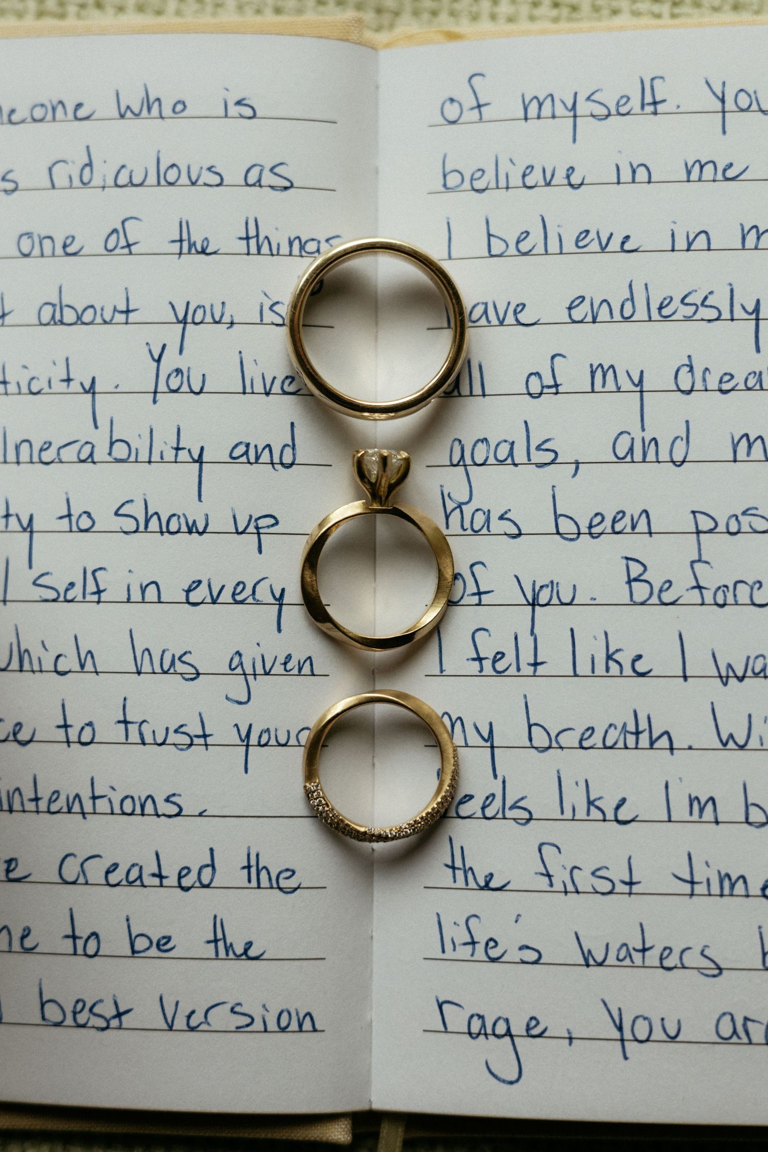 Four gold wedding rings stacked vertically on an open journal with handwritten love letter pages.