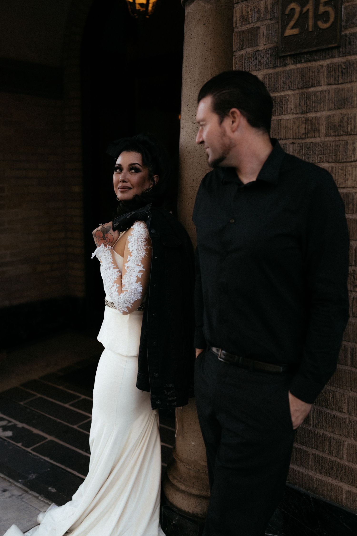 Wedding couple in black and white attire photographed against brick wall.