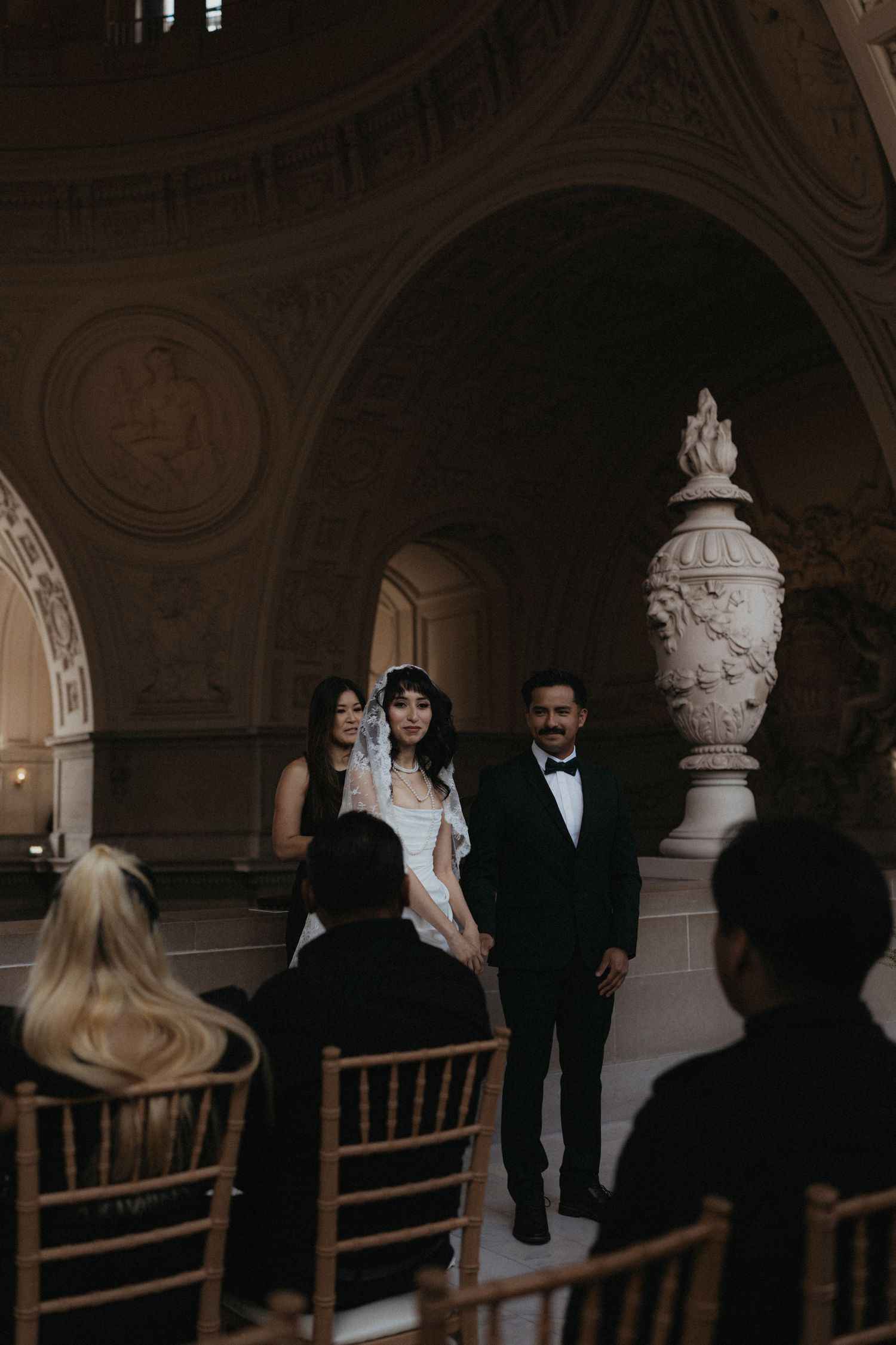Wedding party members gathered in an ornate hallway with classical architectural features.