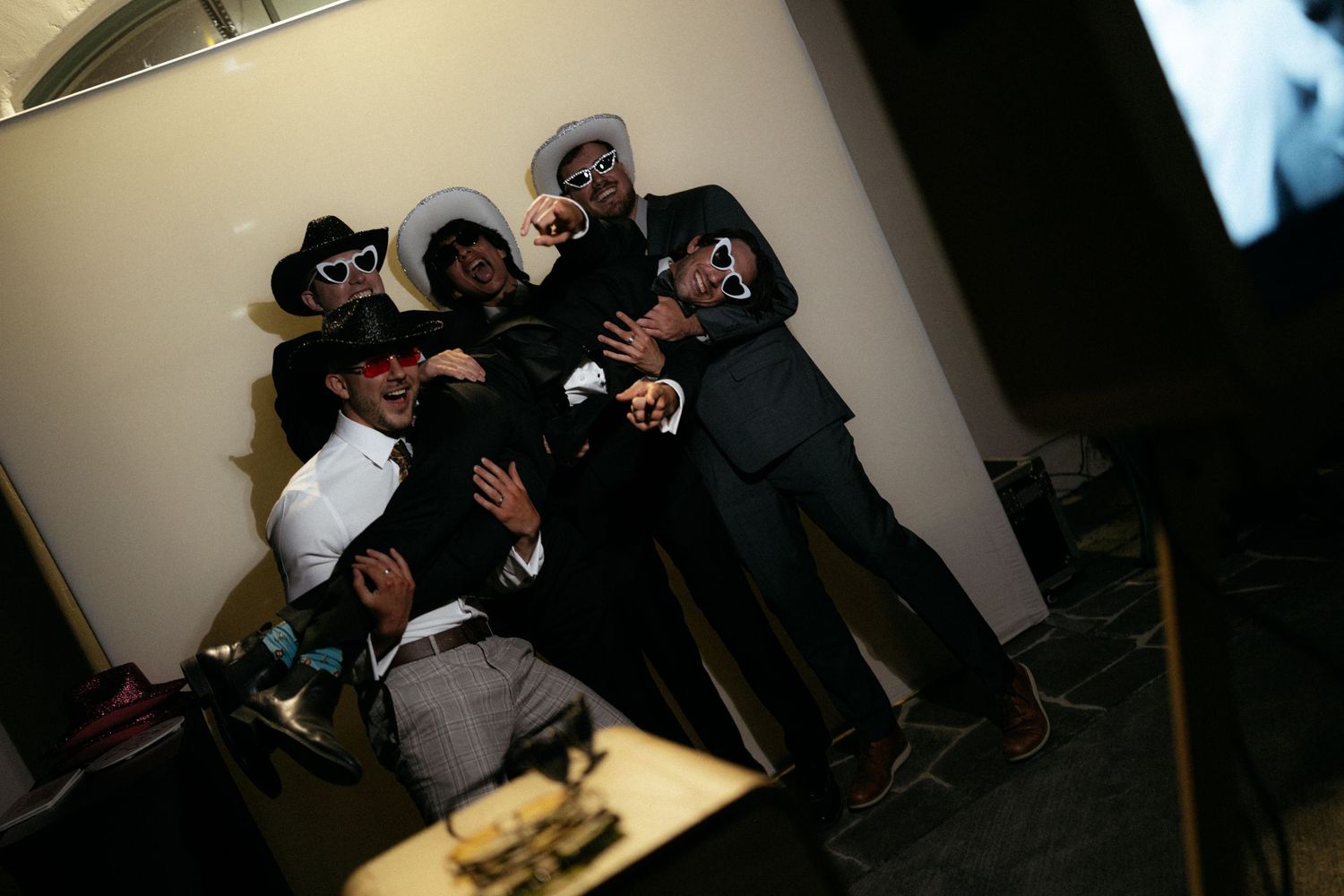 Group of friends posing in hats and sunglasses at a party photo booth, laughing and having fun together.