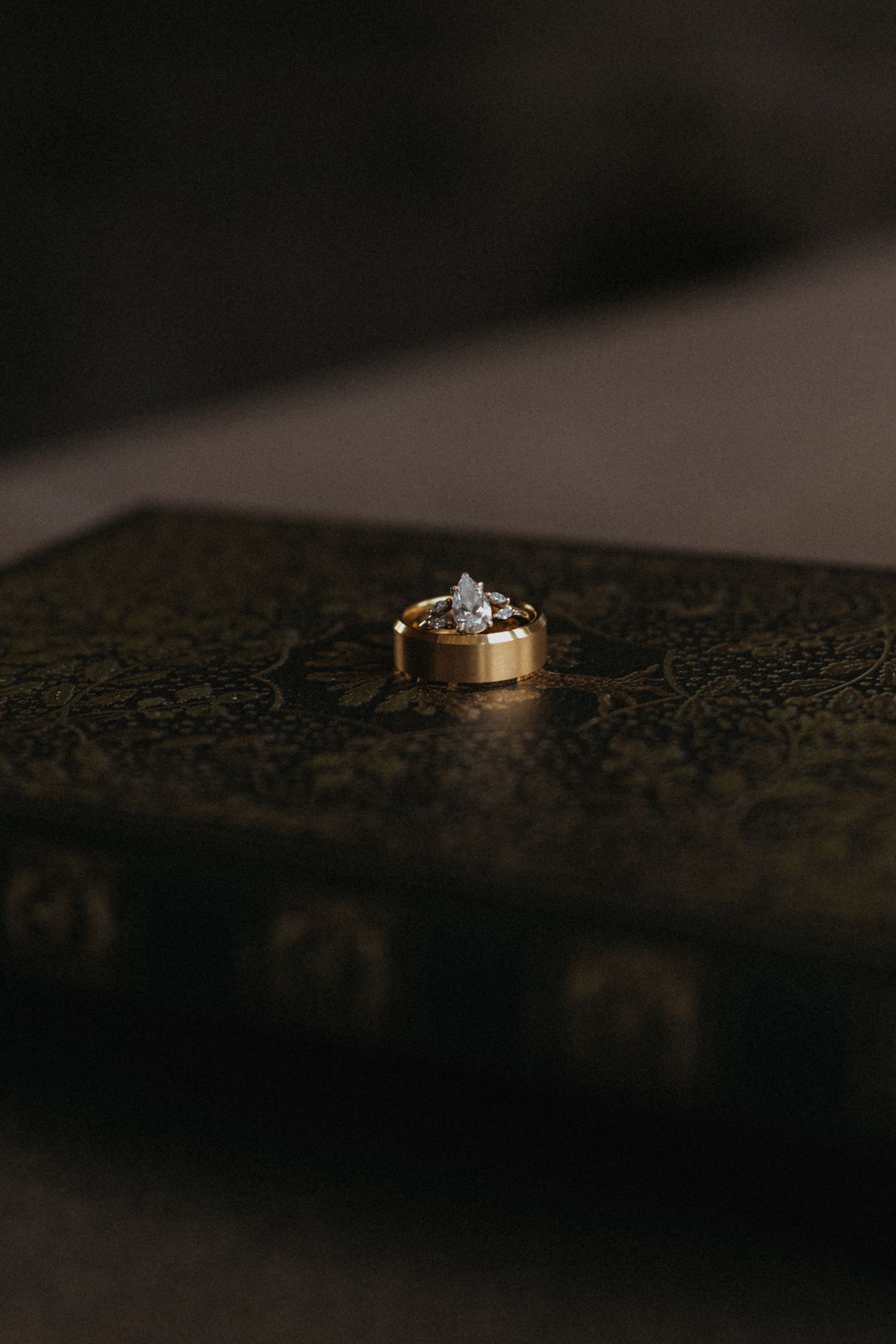 A diamond engagement ring and wedding band rest on a dark textured surface.