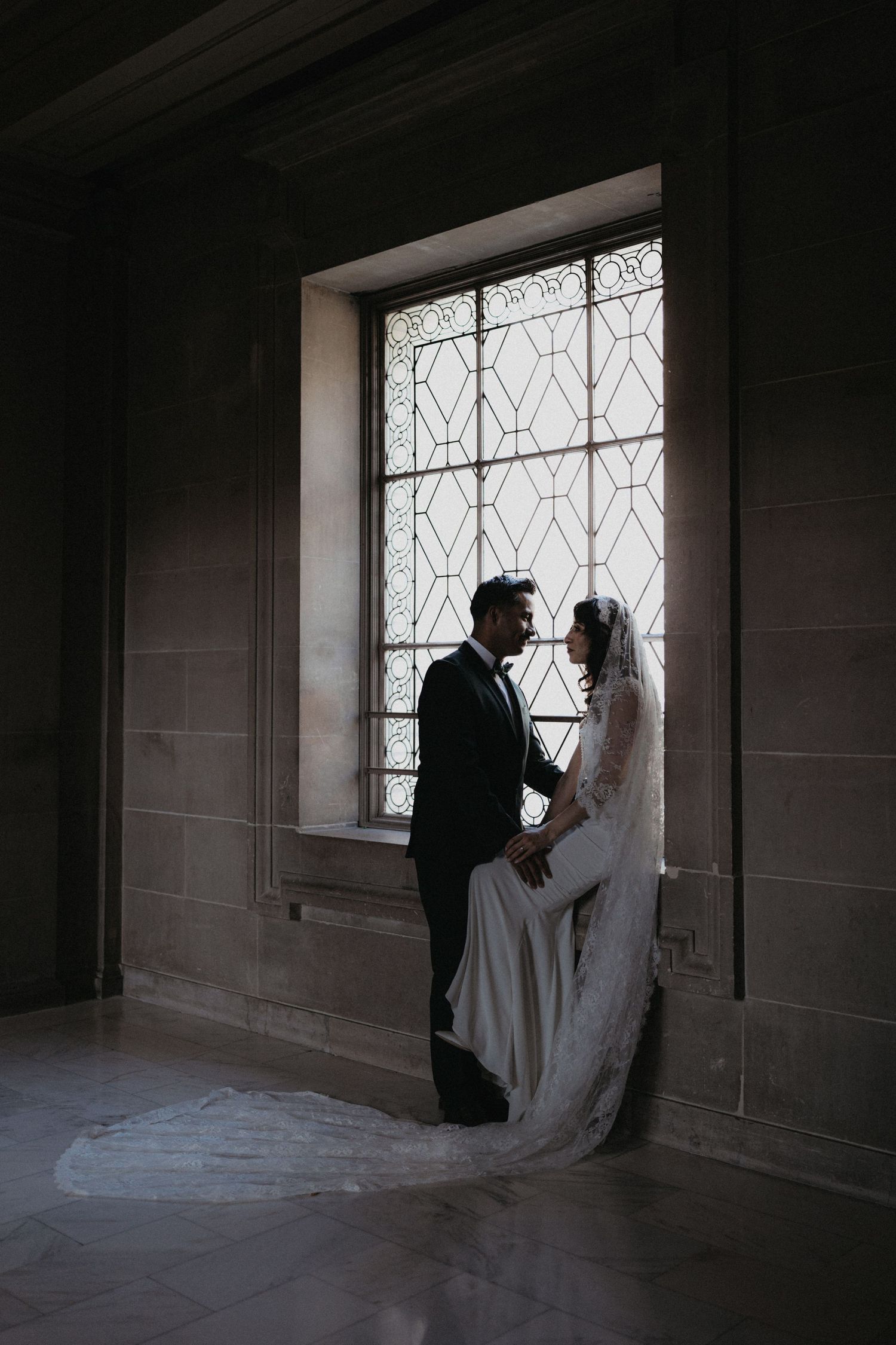 Dramatic silhouettes of newlyweds against a bright window in a stone corridor.