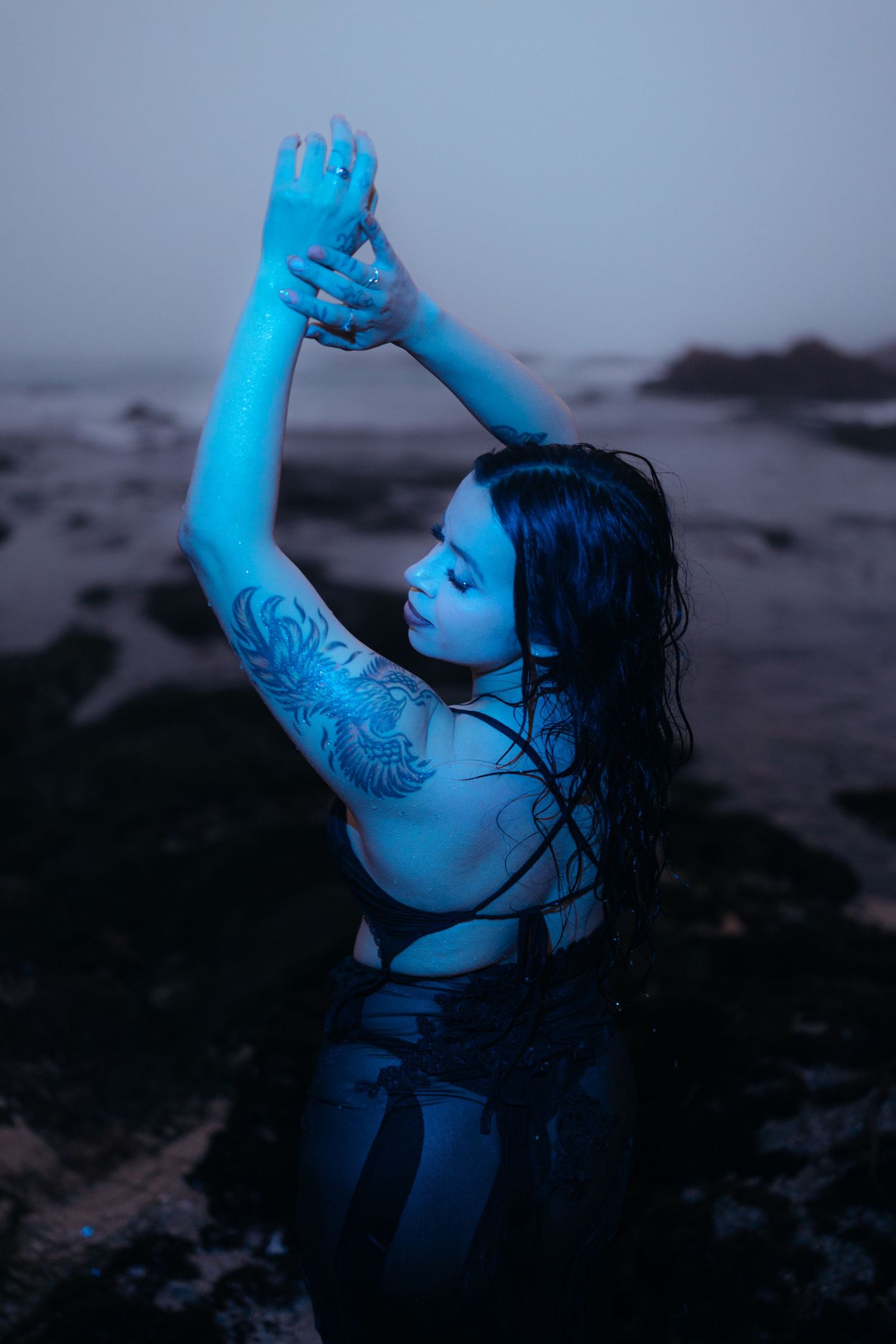 Artistic blue-tinted photo of a dancer posing against a misty coastal backdrop.