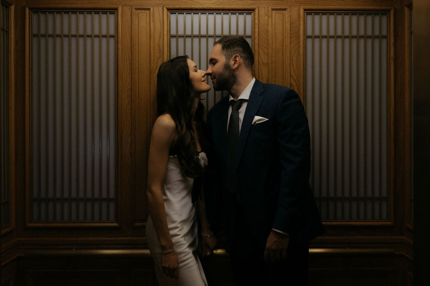 A couple shares an intimate moment in a dimly lit hallway with wood paneled walls.