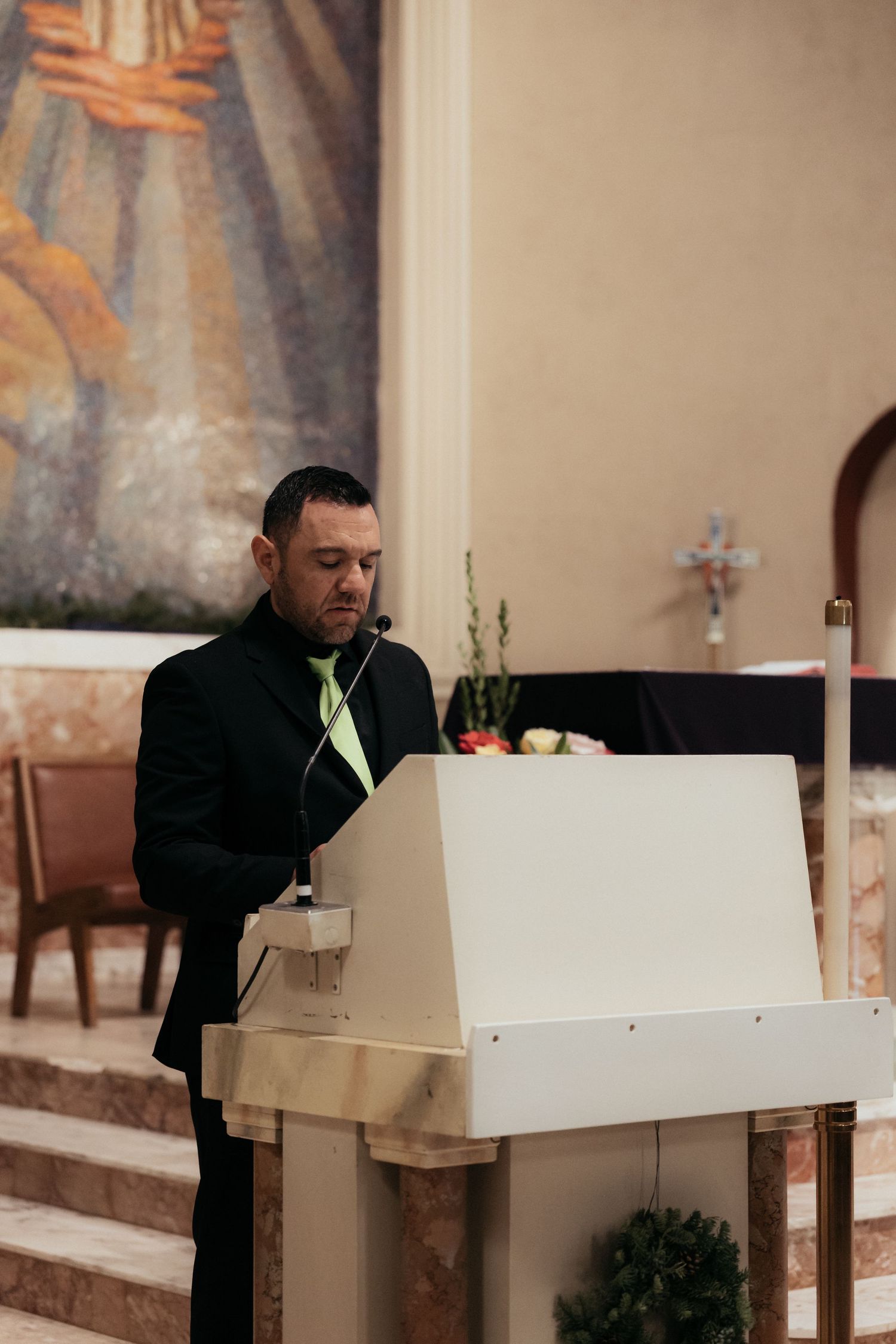 A person in formal attire speaks at a white podium during a church service.