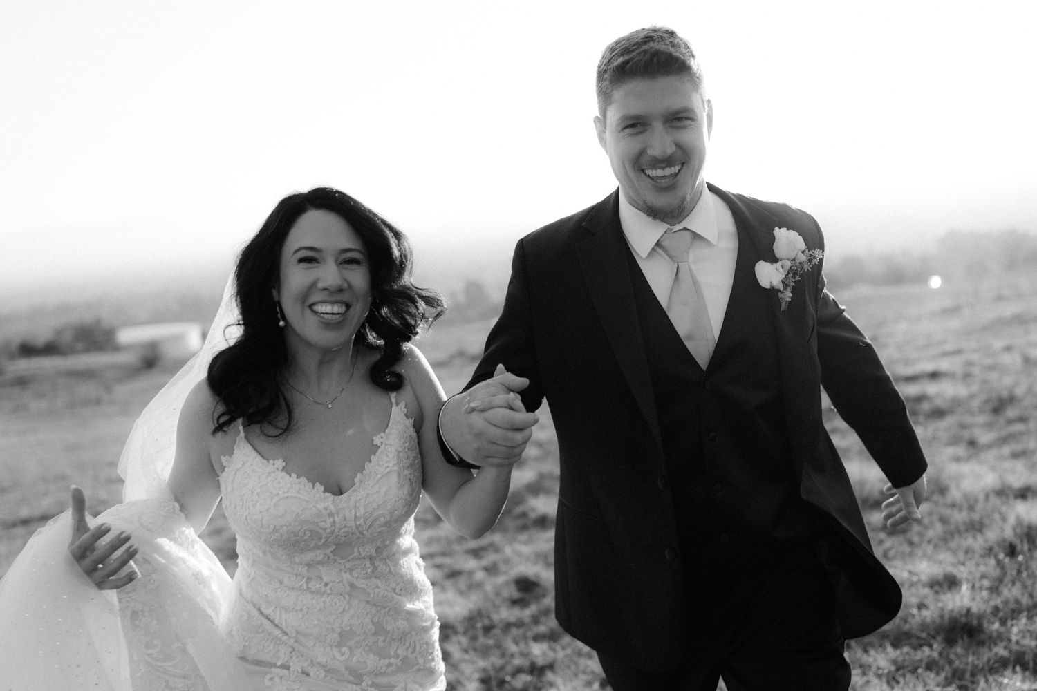 Joyful wedding couple running and laughing together on a hillside.