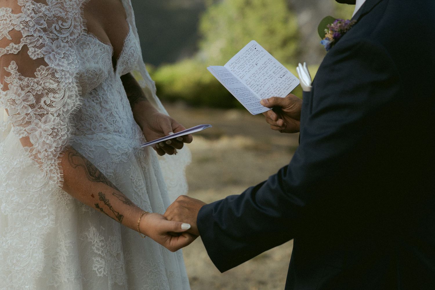 Close-up of bride and groom exchanging wedding vows while holding hands and reading from paper cards.