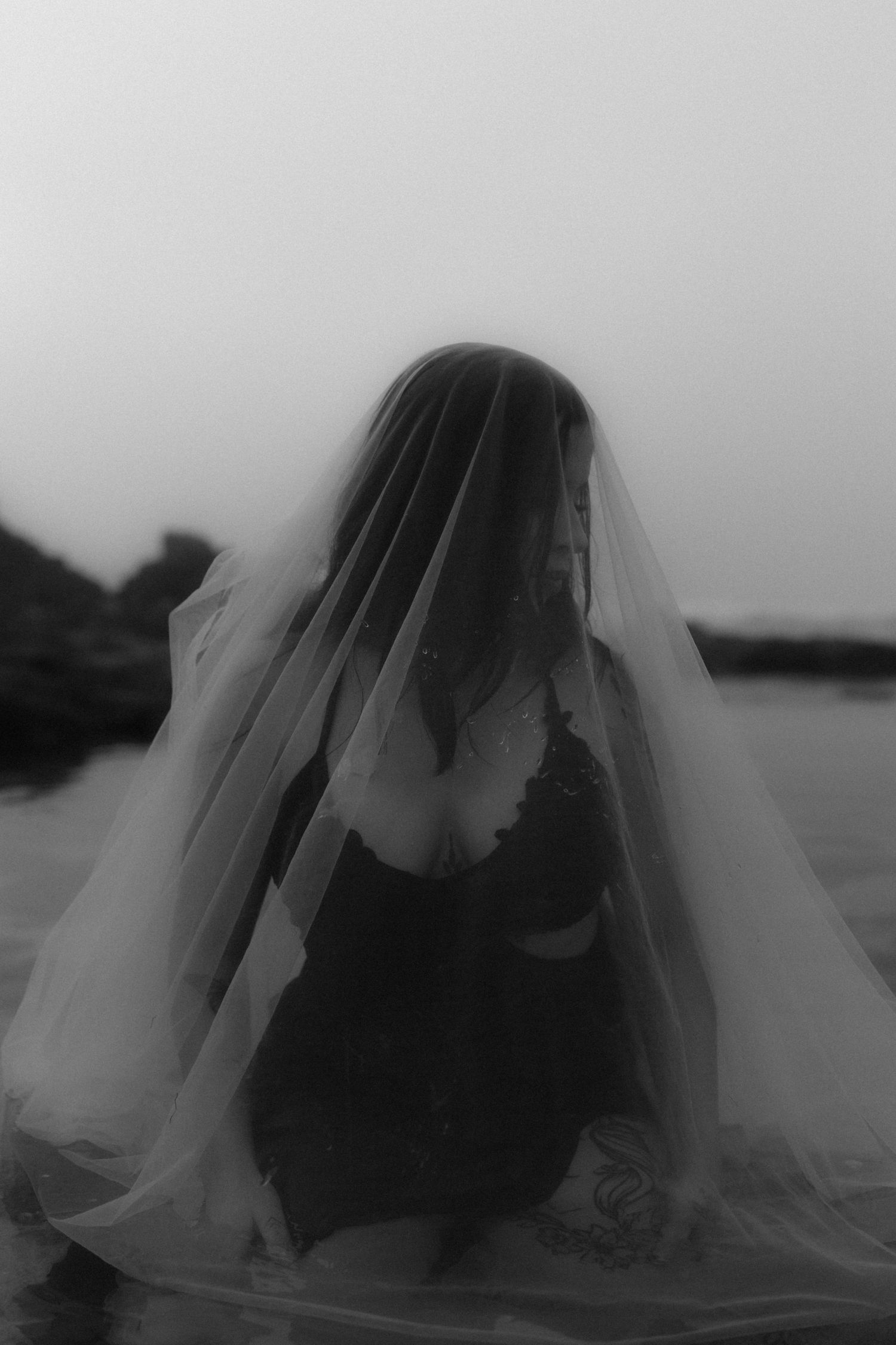 Mysterious form shrouded in translucent white veil against moody seascape.