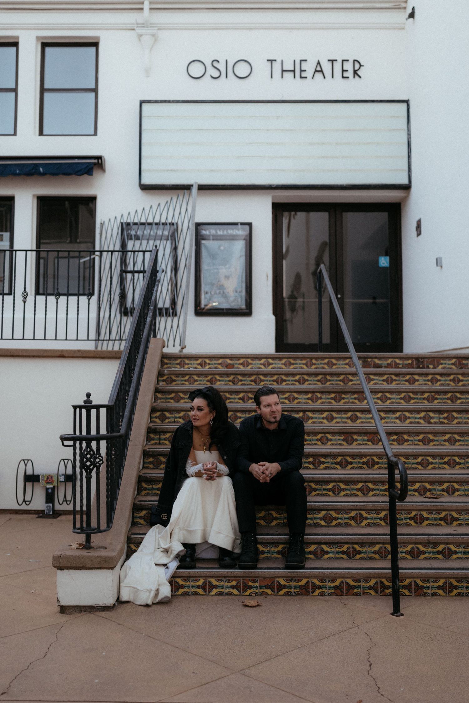 A couple sits on the steps of the Osio Theater with decorative tile work visible.