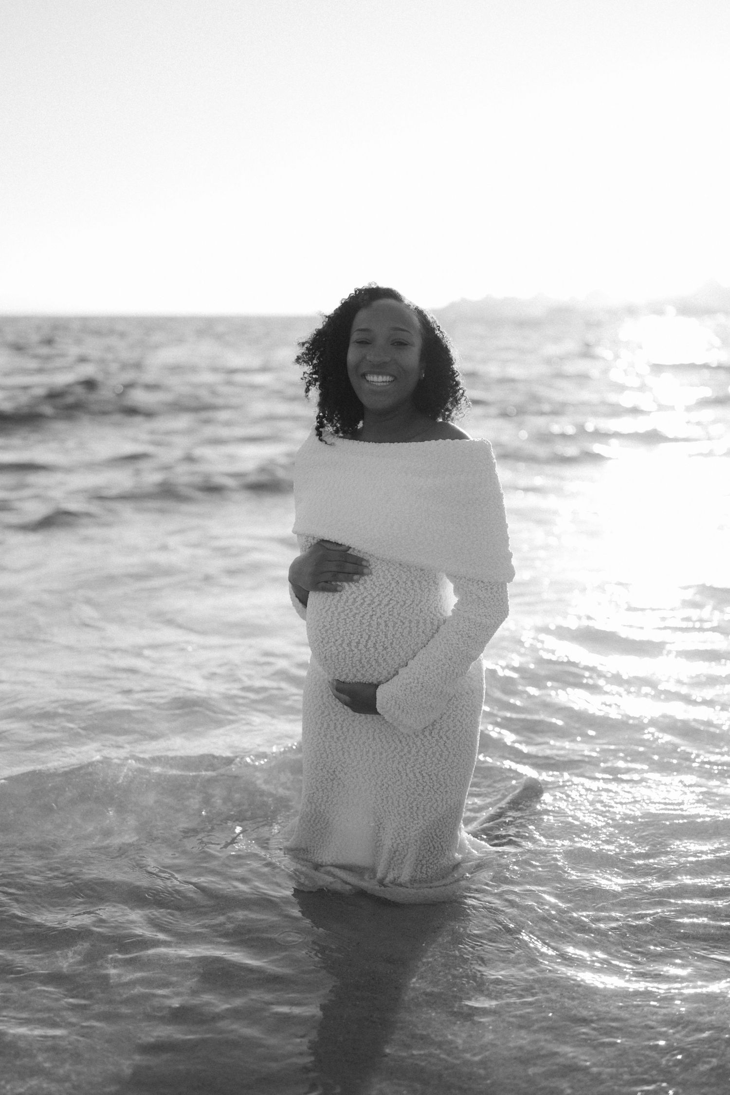 A series of black and white photos shows someone standing in ocean waves wrapped in a white sweater.