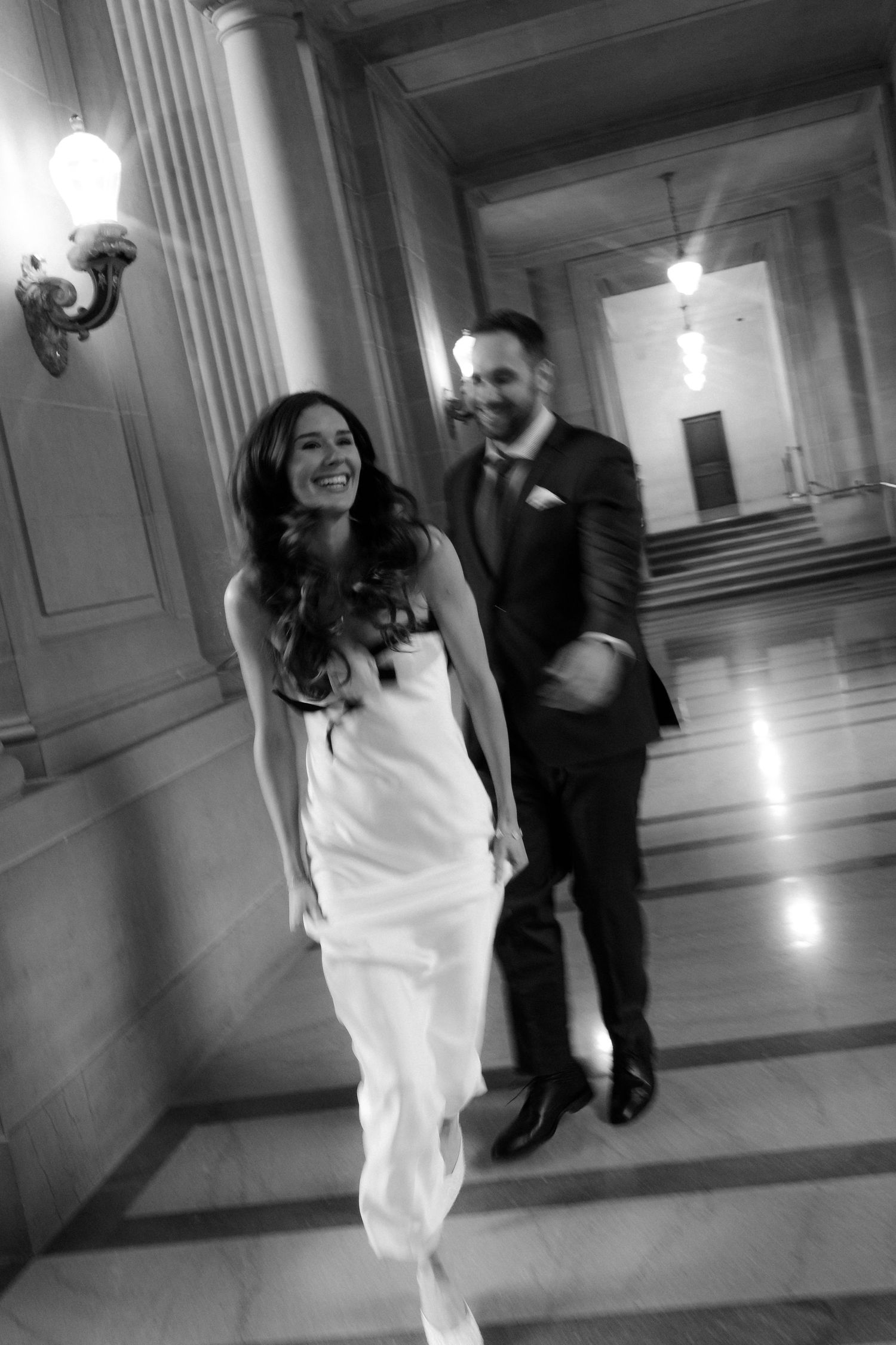 Black and white sequence of a couple dancing and twirling in an elegant hallway with ornate wall sconces.