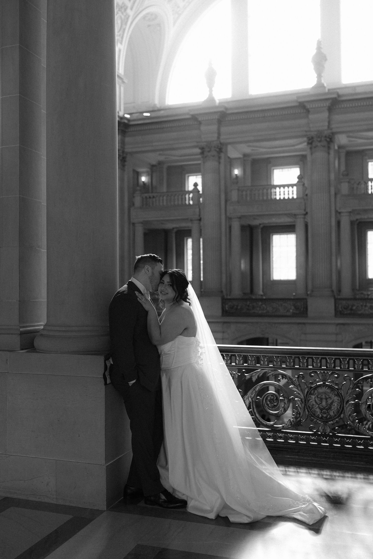Black and white photo series showing a couple in wedding attire posing along an elegant indoor balcony with columns.