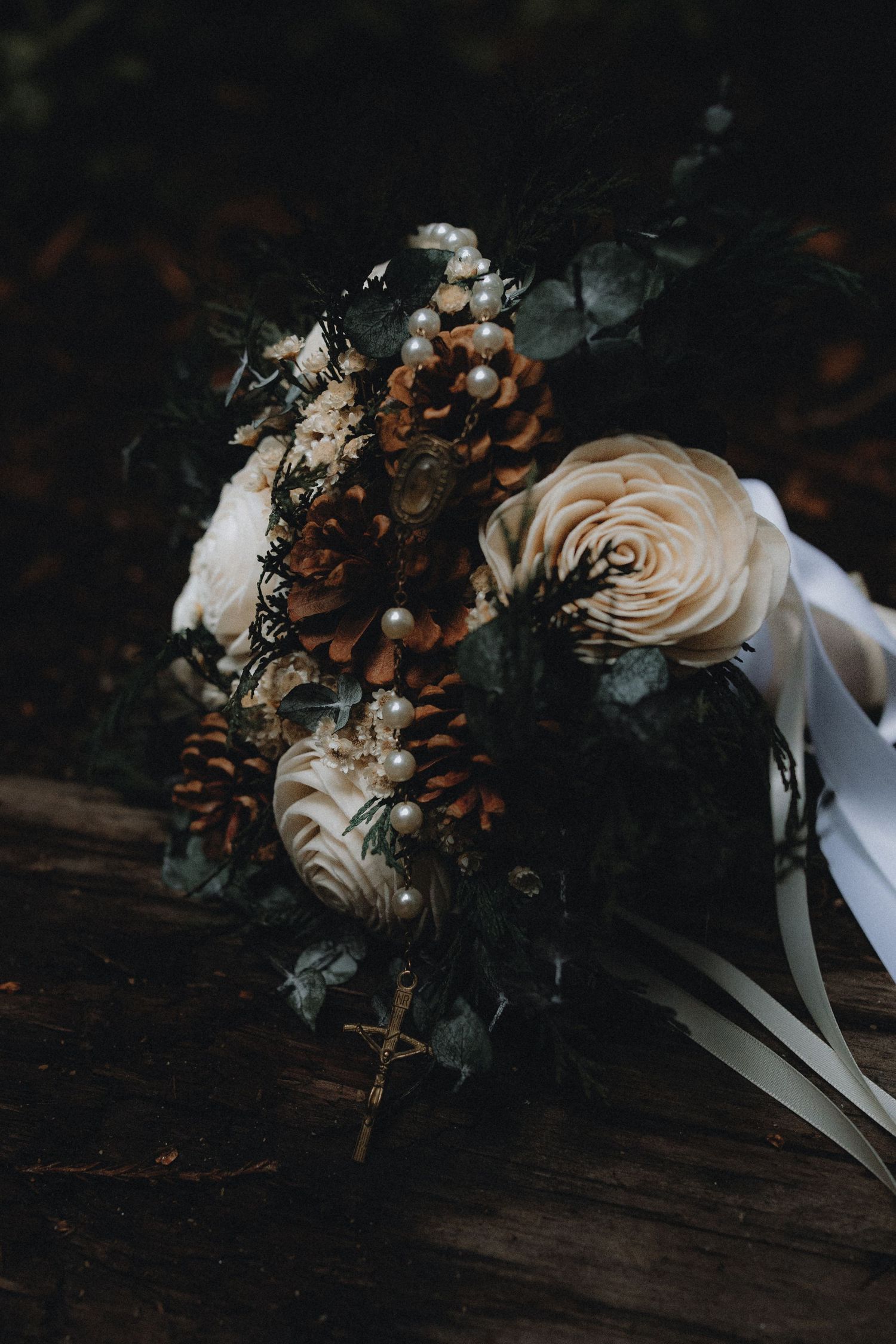 A series of moody, dark photographs showing dried roses with white ribbons arranged against a rustic wooden surface.