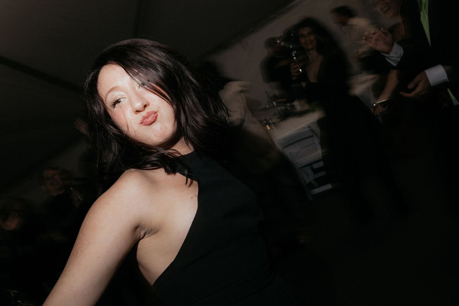 Wedding guests dance and celebrate on a dimly lit dance floor under a tent.