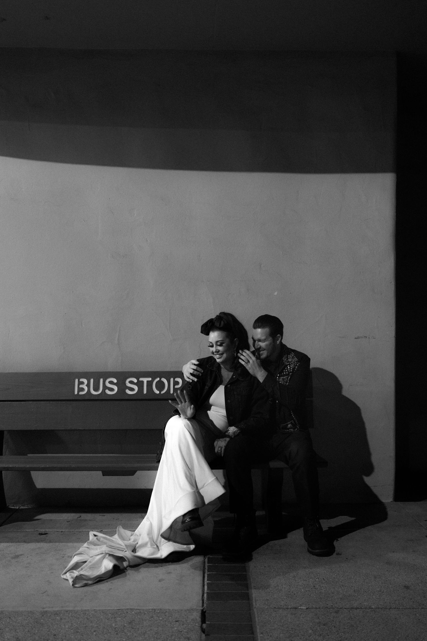 A couple rests near a bus stop sign in an artistic black and white composition.