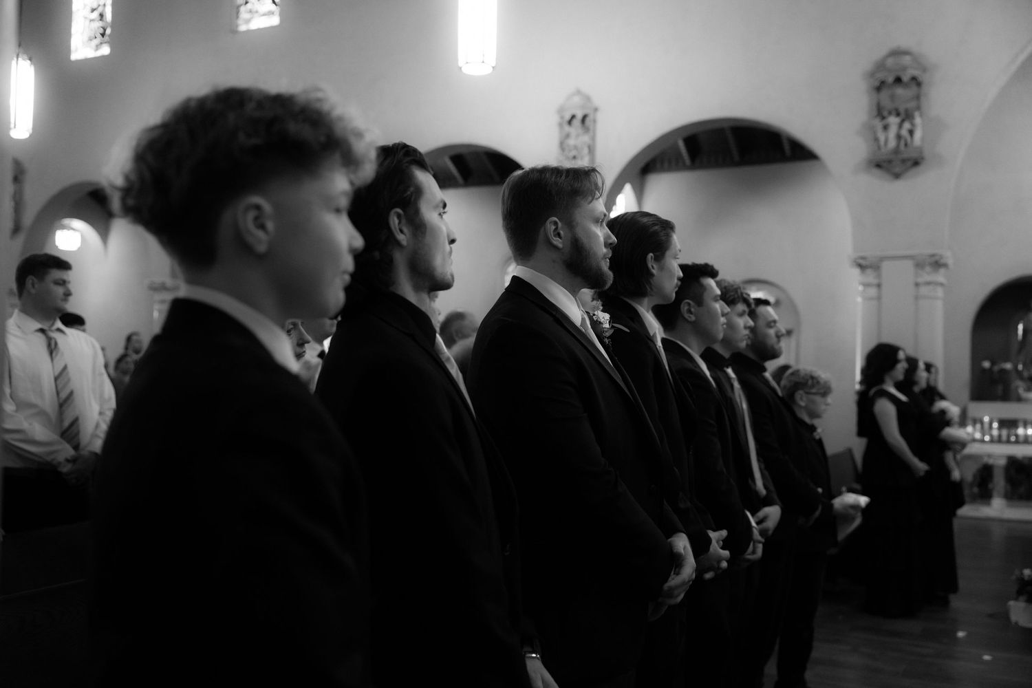 Silhouetted wedding guests watching ceremony in church with dramatic lighting.