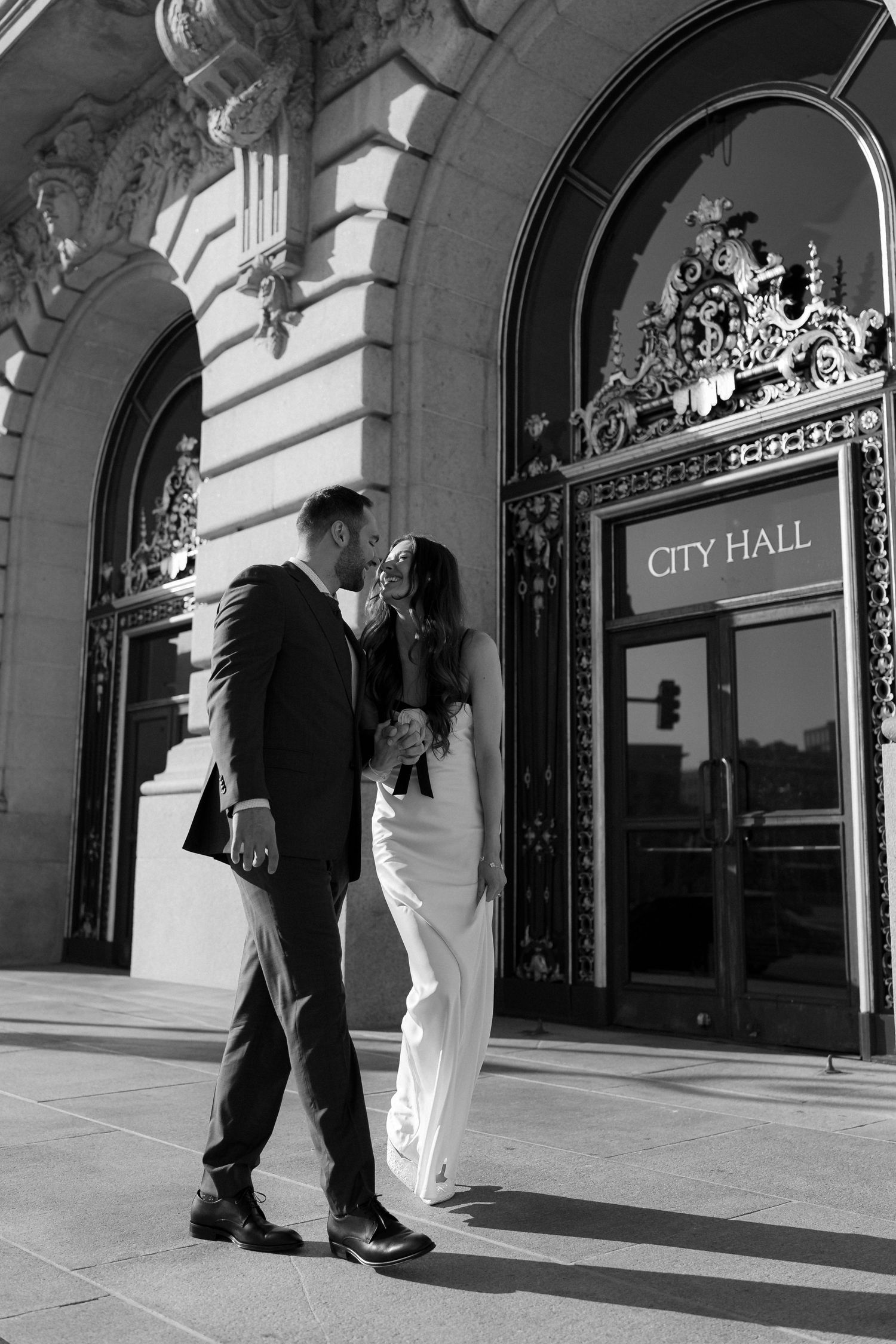 A couple walks together outside City Hall with ornate architectural details visible in the background.