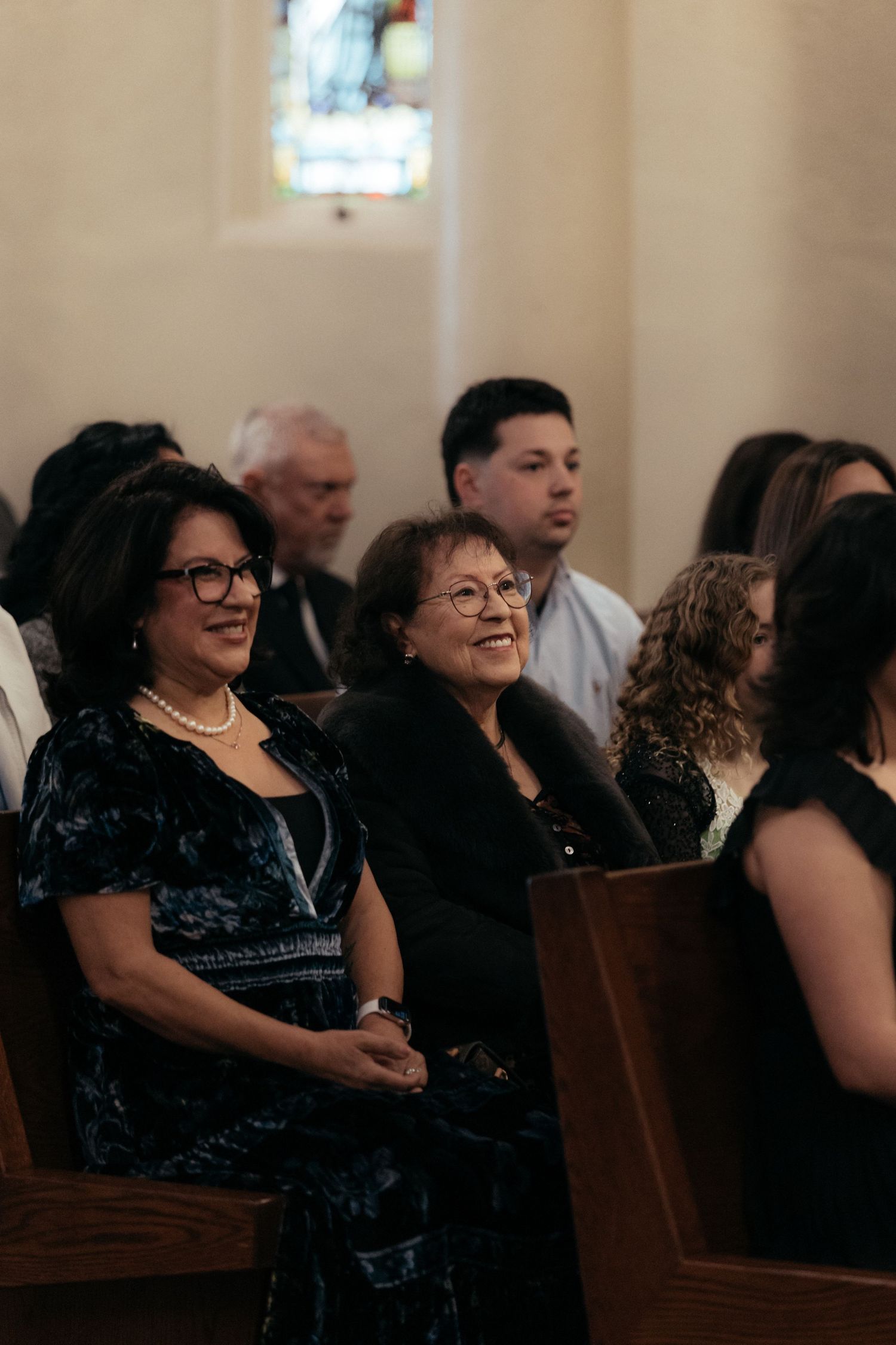 Wedding guests smile and watch the ceremony from church pews.