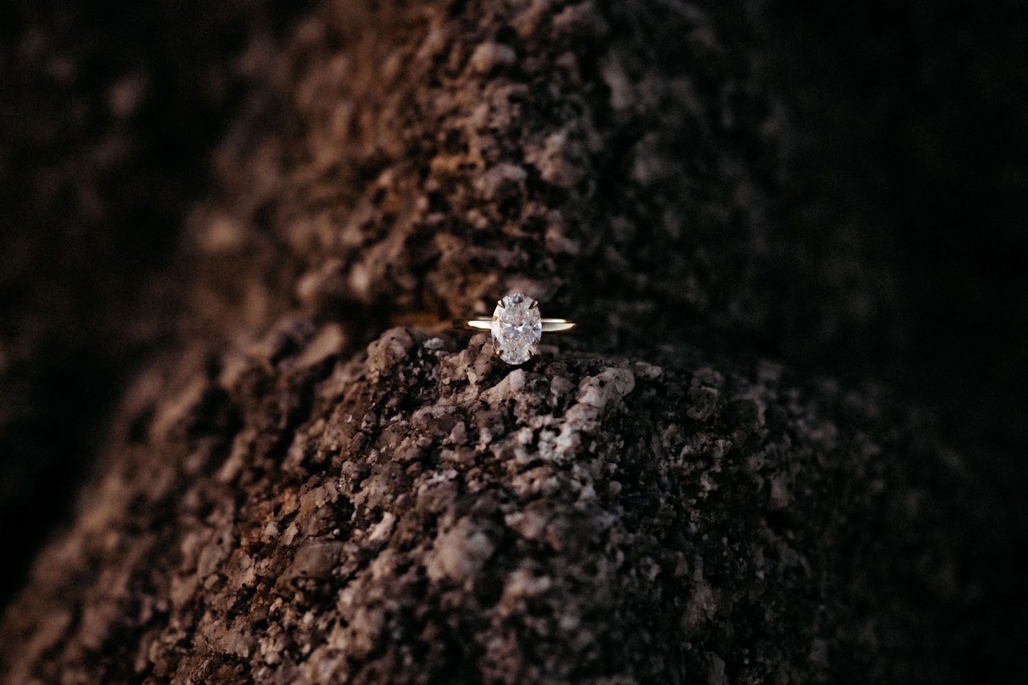 A sparkling diamond engagement ring with halo setting resting on dark textured rock surface.