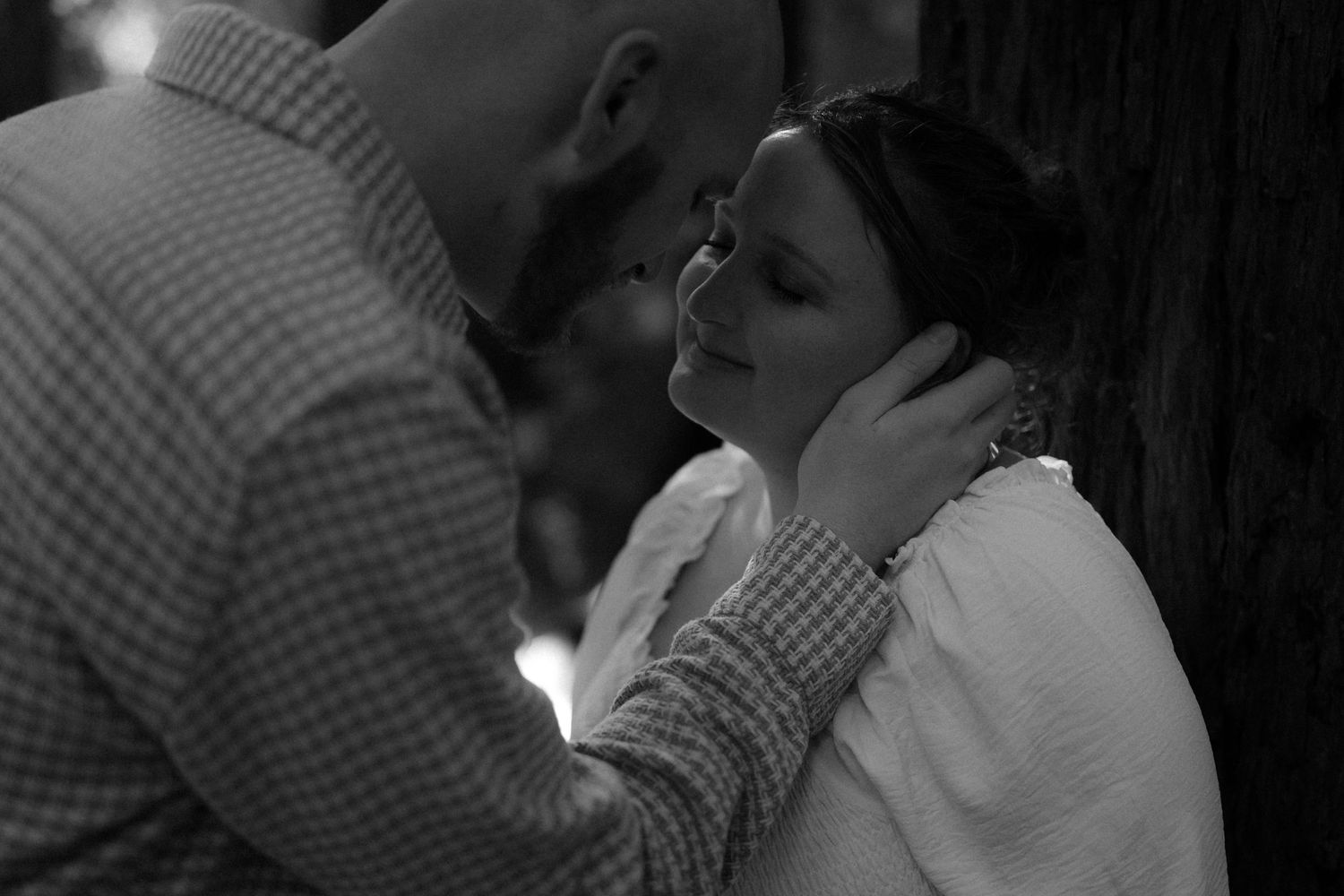 A tender black and white photograph captures an intimate moment between two people in soft lighting.