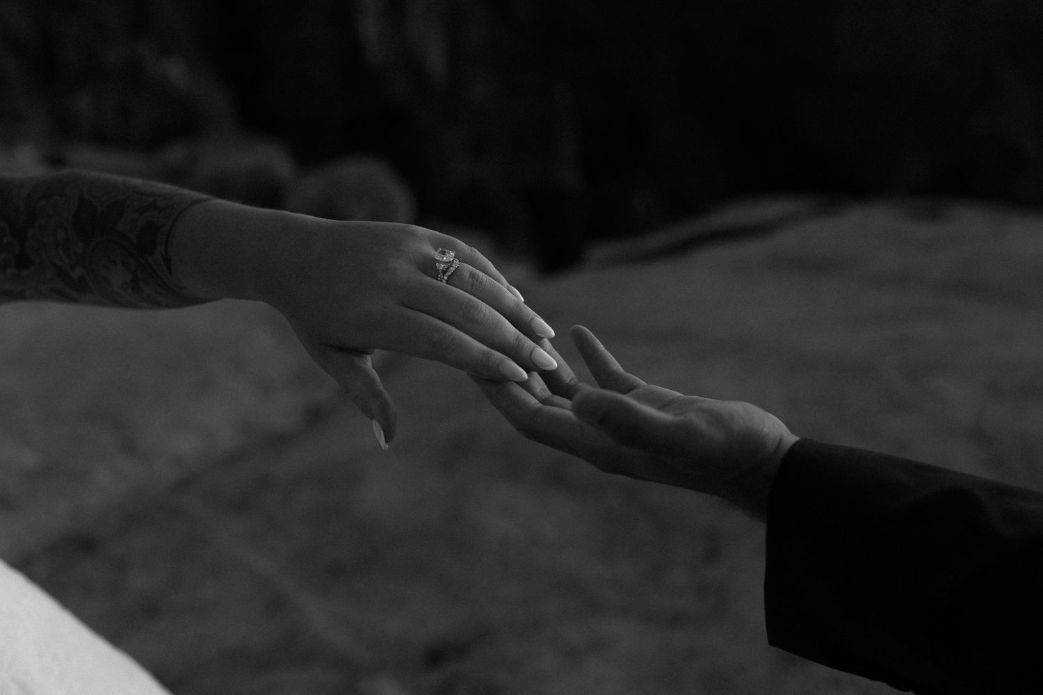 Black and white close-up of bride and groom touching hands, showing wedding ring during ceremony.