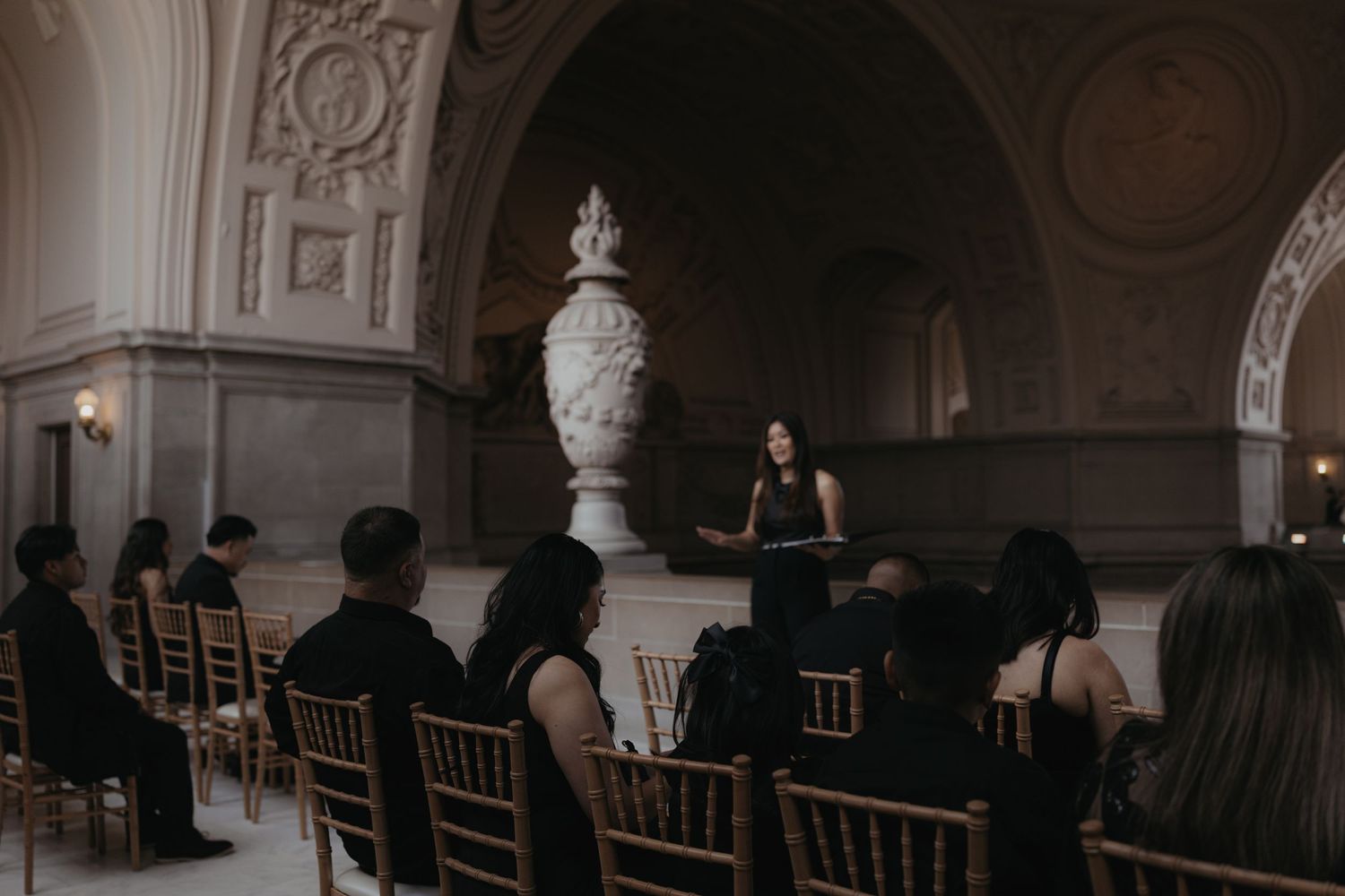 A performance in a grand hall with ornate white vases and classical architecture.