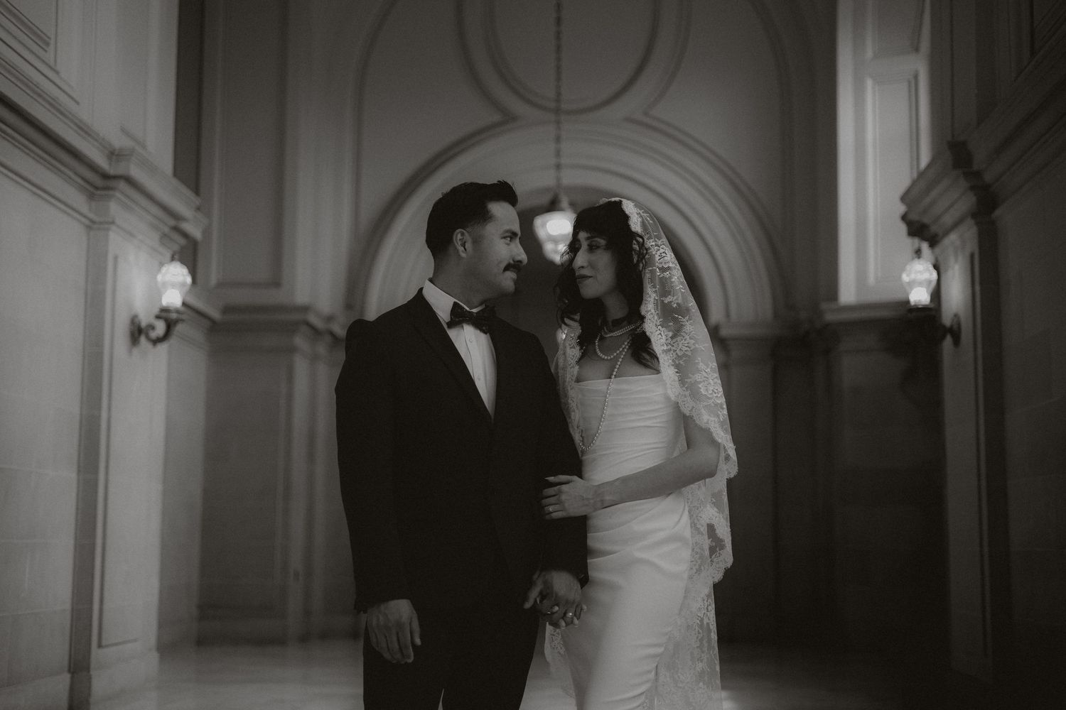 Wedding couple poses in an elegant arched hallway with dramatic natural lighting.