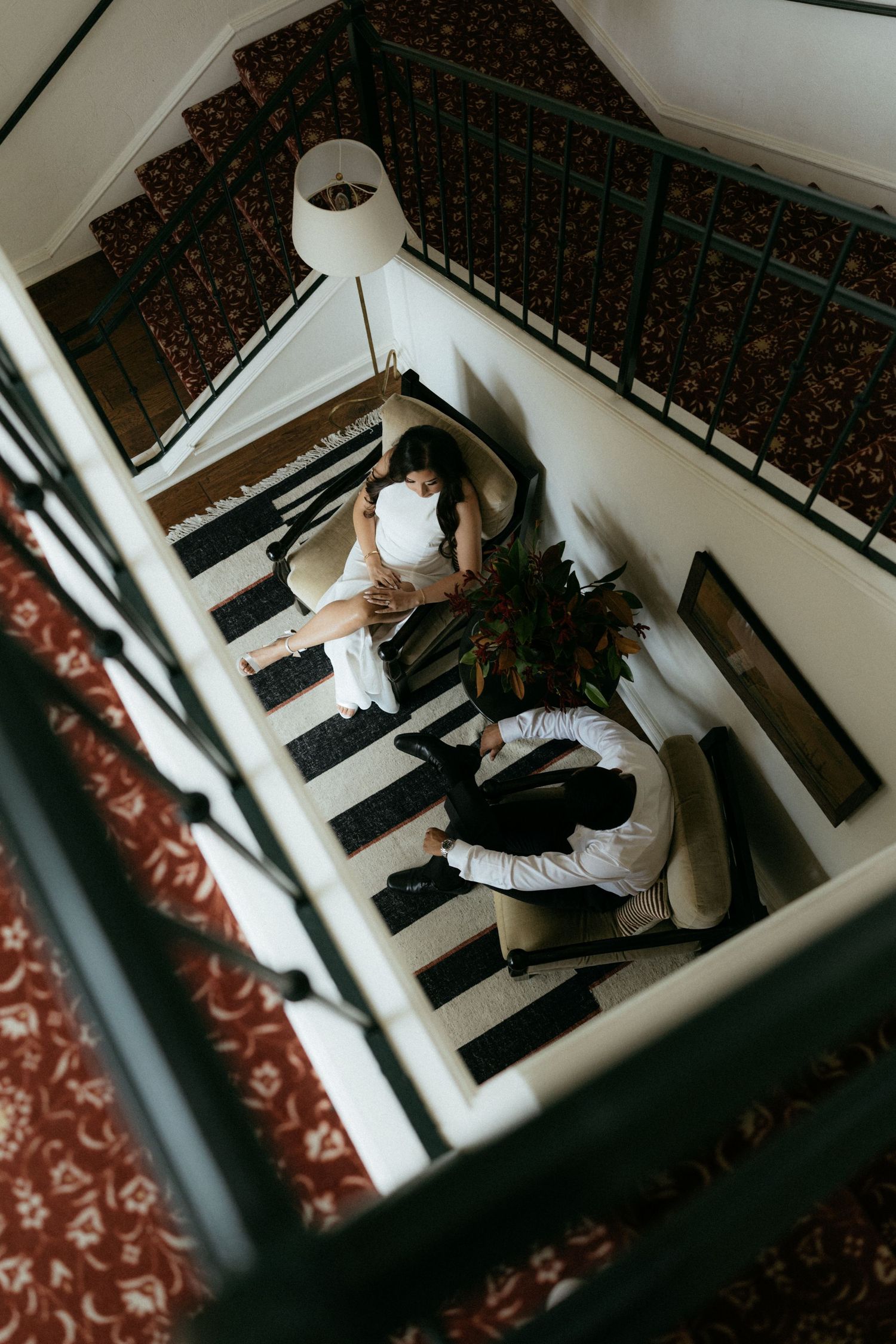 Aerial view of couple relaxing in elegant hotel lobby with striped floors and red patterned carpets.
