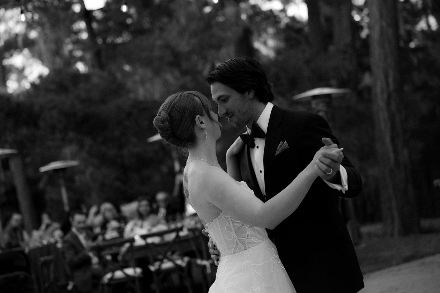 Bride and groom sharing romantic first dance outdoors in black and white wedding photo.